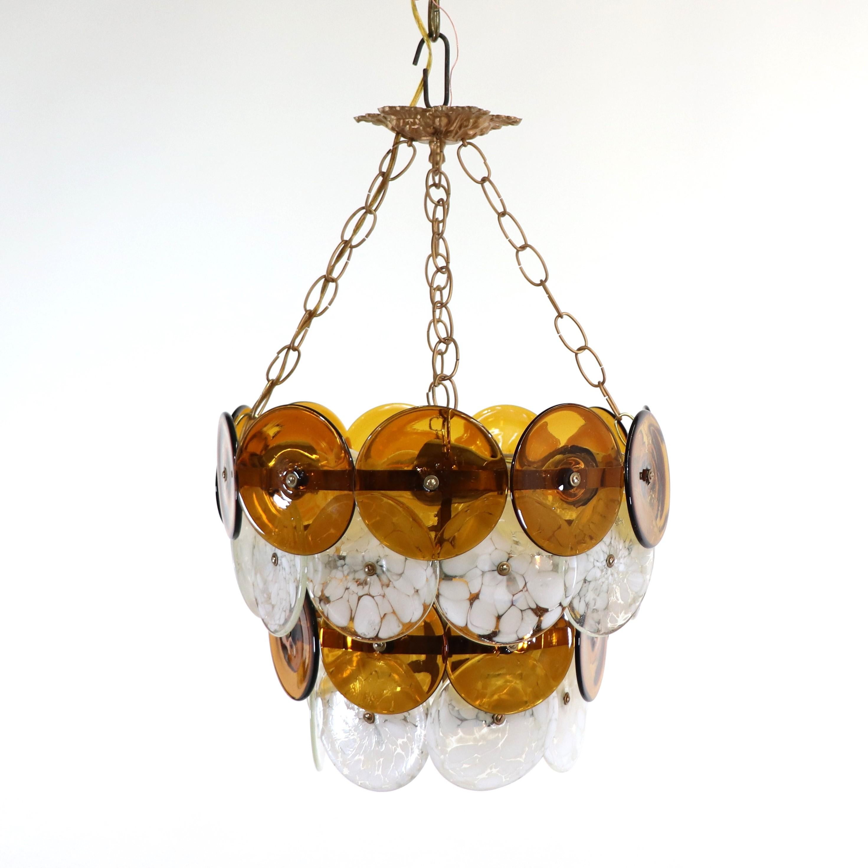 Questo lampadario in vetro di Murano della metà del secolo scorso ha quattro livelli di dischi montati su una struttura in ottone con un dettaglio di foglie d'acanto. I dischi sono elementi soffiati a mano singolarmente, con i livelli che si