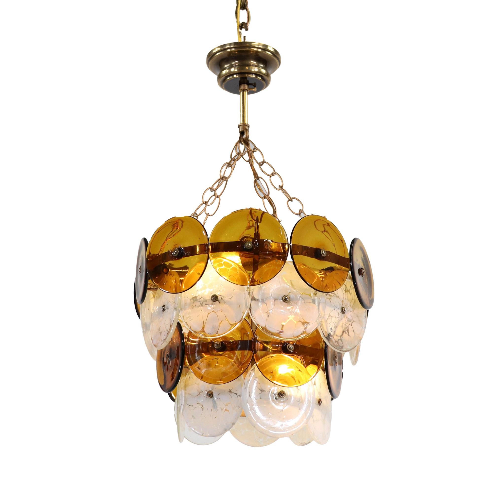 This mid-century Murano glass chandelier has four tapered tiers of alternating amber glass discs with white and clear glass disks with a marbleized design. The discs are individually handblown elements. The marbleized design is a combination of