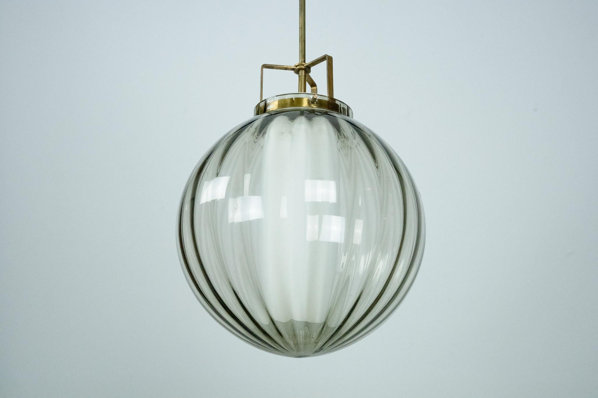 Elegant lustre du milieu du siècle, avec un globe extérieur en verre soufflé de Murano en finition fumée. A l'intérieur, un diffuseur cylindrique en verre opalin distribue la lumière en douceur. Cette pièce allie un savoir-faire italien raffiné à un