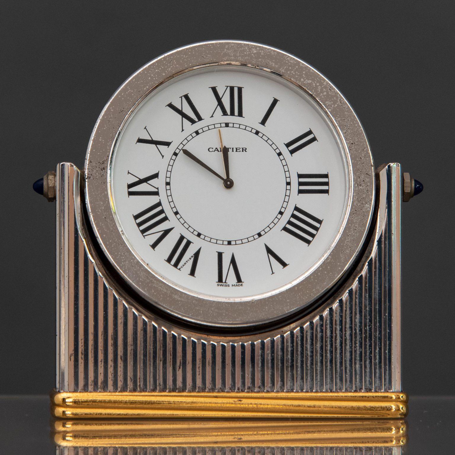 Table alarm clock, steel and brass tilting frame, white dial with Roman hour markers, quartz movement and two cabochon sapphires on the sides.

Cartier Must de Cartier Swiss Made

Serial number 901602199.