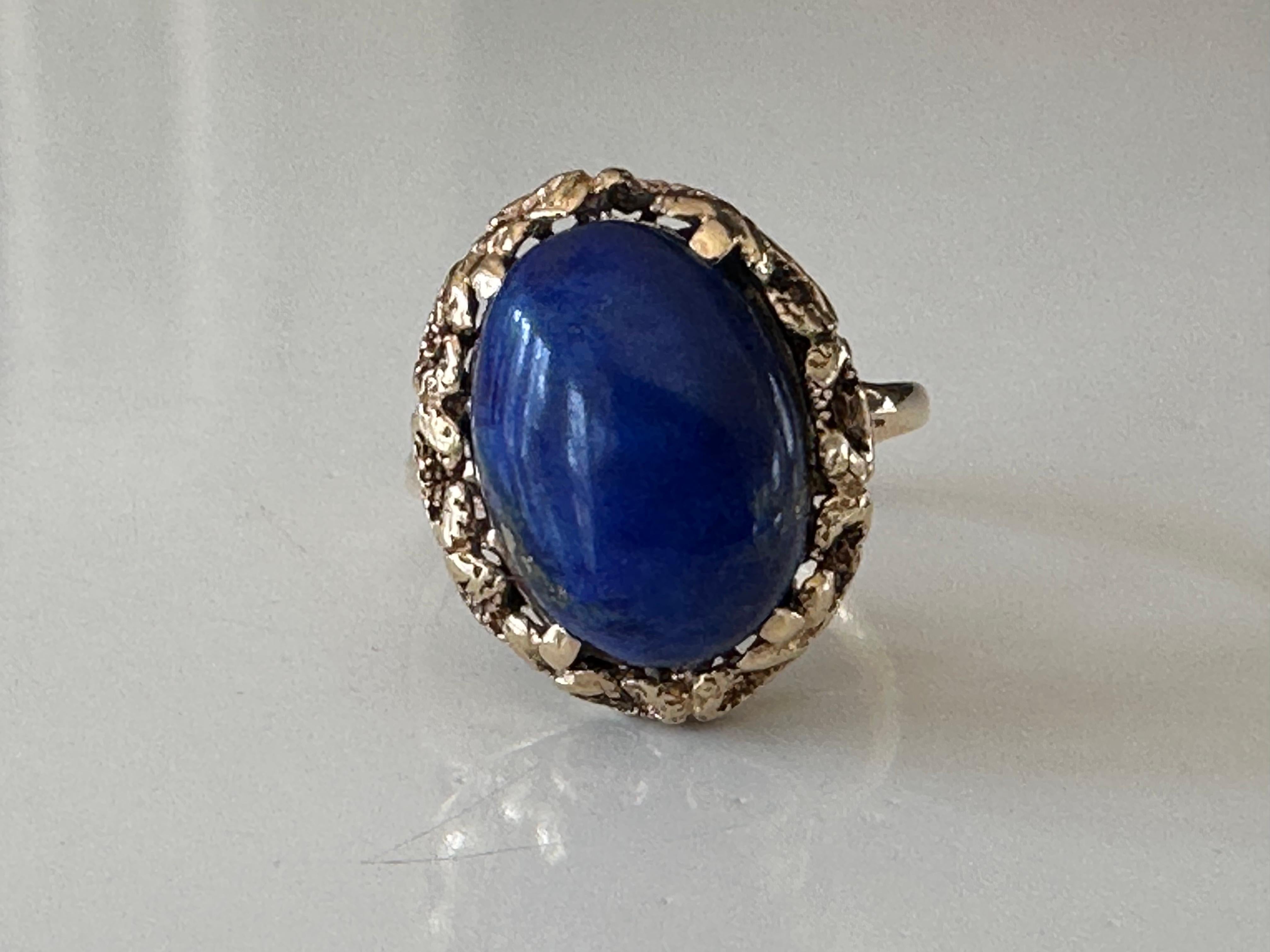 Crafted in the 1950s, this striking vintage cocktail ring is set with a natural lapis lazuli oval-shaped cabochon measuring 11.09 X 15.39mm and weighing approximately 8.59 carats. It is mounted in 14k yellow gold with delicate piercing. 
