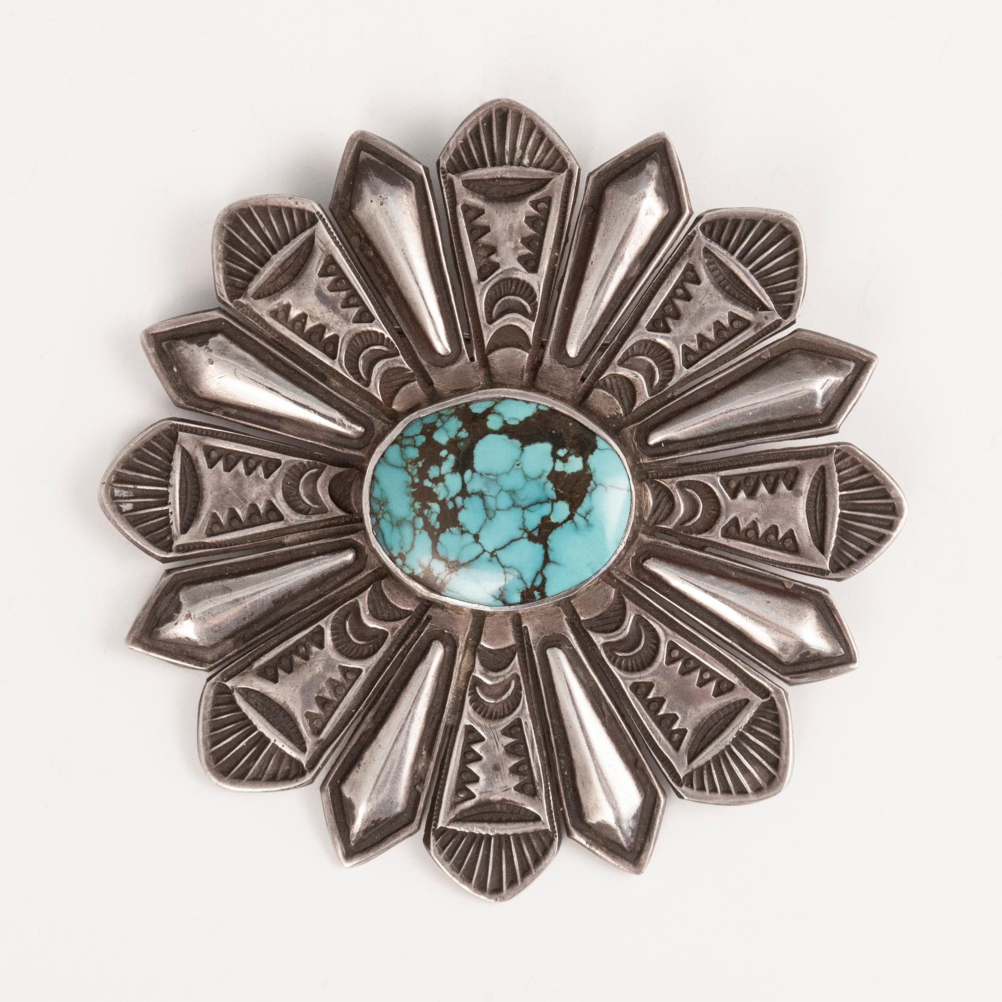 20th century Navajo Silversmith Harry Begay Turquoise and Silver Brooch

A beautiful bezel-set turquoise stone is at the center of this finely stamped sunburst brooch by Navajo silversmith Harry H. Begay. Marked with initials HHB over a left