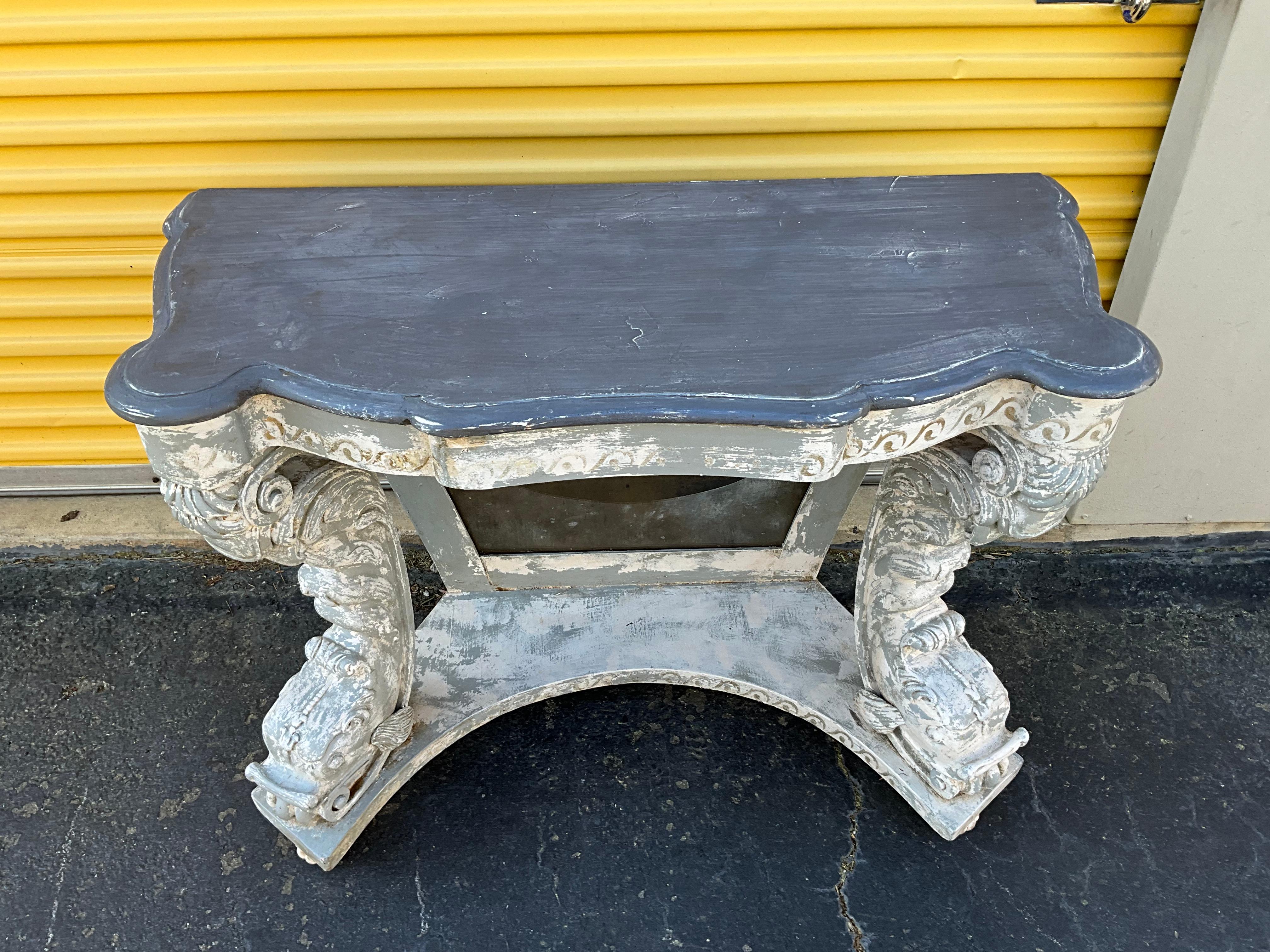 This is a pair of neo-classical style carved and hand painted console tables with distressed mirrored backs. The top has a serpentine form . The bases have dolphin / koi fish supports. They most likely are Italian mid-century finds. The consoles are