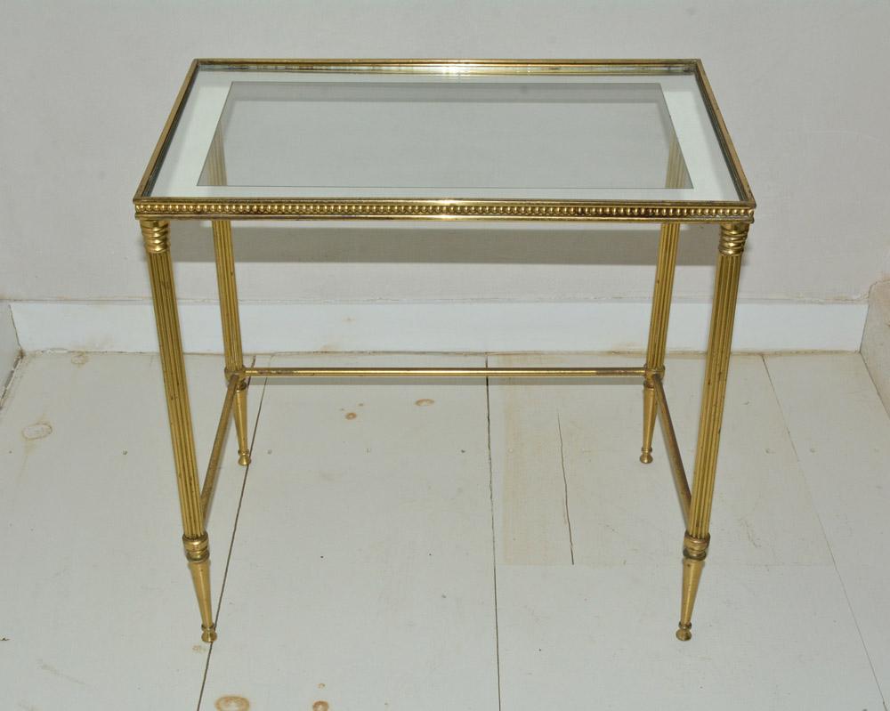 The midcentury neoclassical Maison Jansen style brass side or end table has a silver band glass top framed with a beaded edging, fluted legs and tapered feet. There are brass stretchers on three sides so that the table can be pulled up to a seated