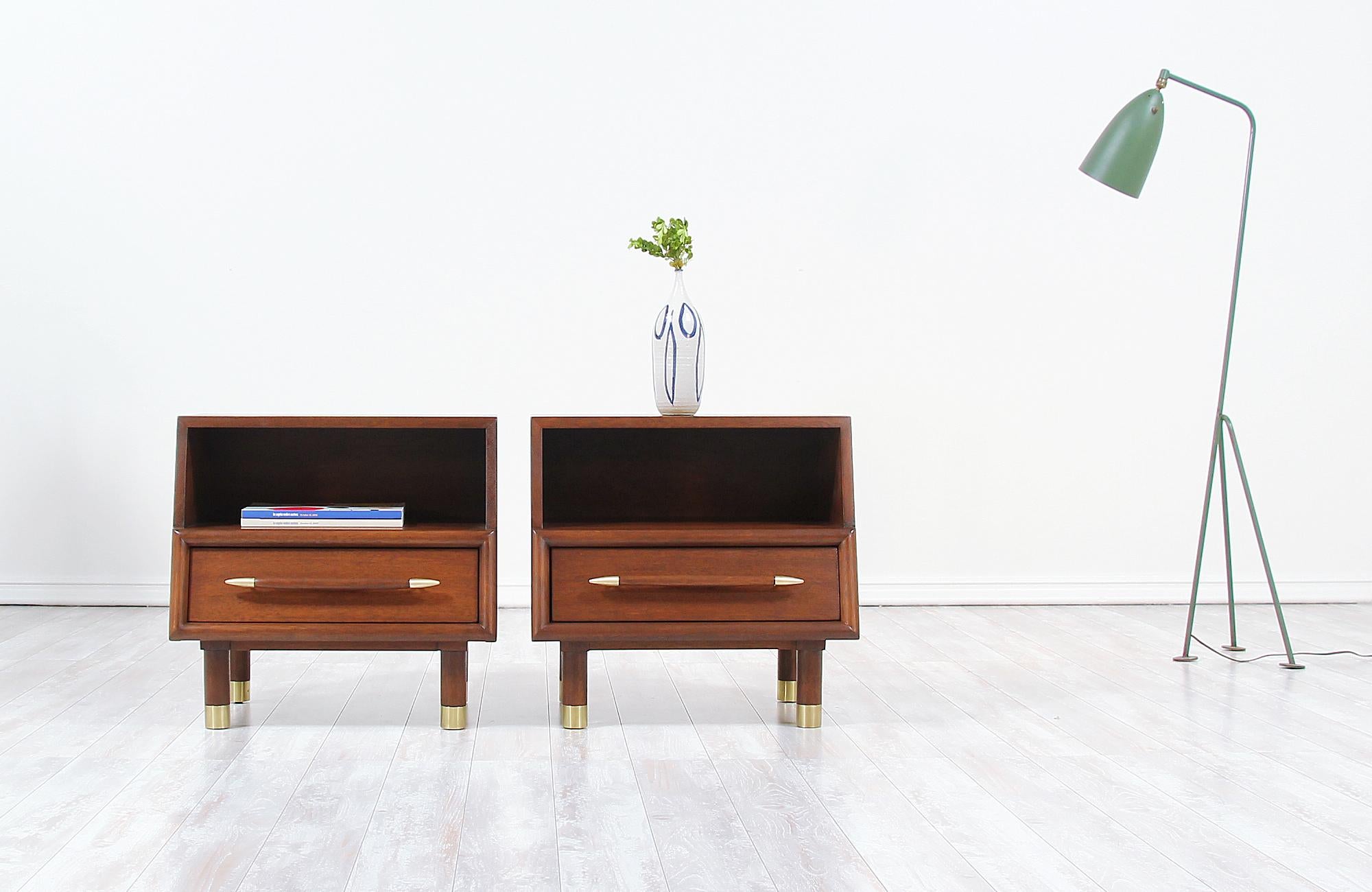 A pair of elegant nightstands designed by John Keal for Brown Saltman in the United States circa 1950s. This fabulous pair of nightstands are built on solid walnut-stained mahogany wood featuring polished brass accents on the edge of the drawer