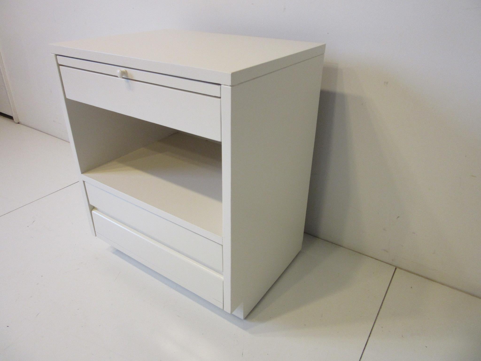 A bone white painted wooden nightstand or chest with top pull out, small drawer, storage area and larger drawer to the bottom. Retains the manufactures branded mark by the Sligh Furniture company from their Cross Country collection.