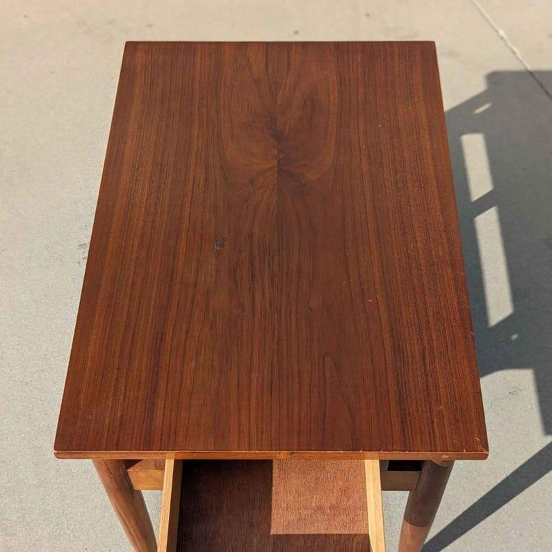 Cette table de nuit Mid Century de Red Lion Table Co est un ajout élégant et pratique à toute chambre à coucher. Fabriquée en bois massif et en placage de bois avec un design rétro des années 60, cette pièce polyvalente peut être utilisée comme