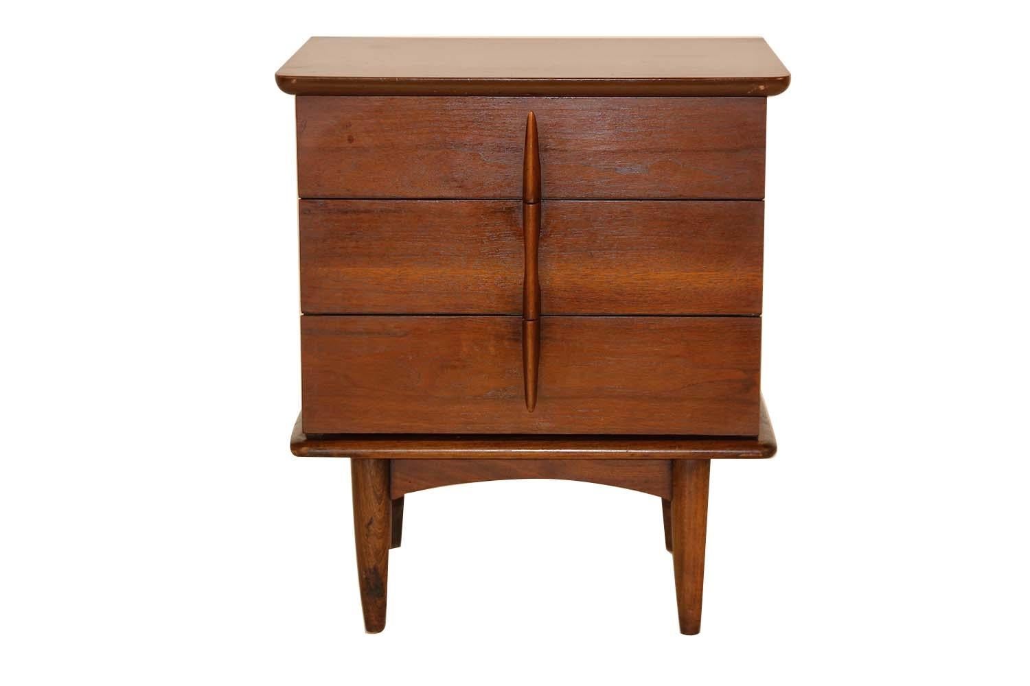 A remarkable midcentury nightstand/side table by United in nearly pristine condition. Exceptional construction and style, features three dove tailed spacious drawers accented with beautiful sculpted pulls. The nightstand rest over tapered legs. This
