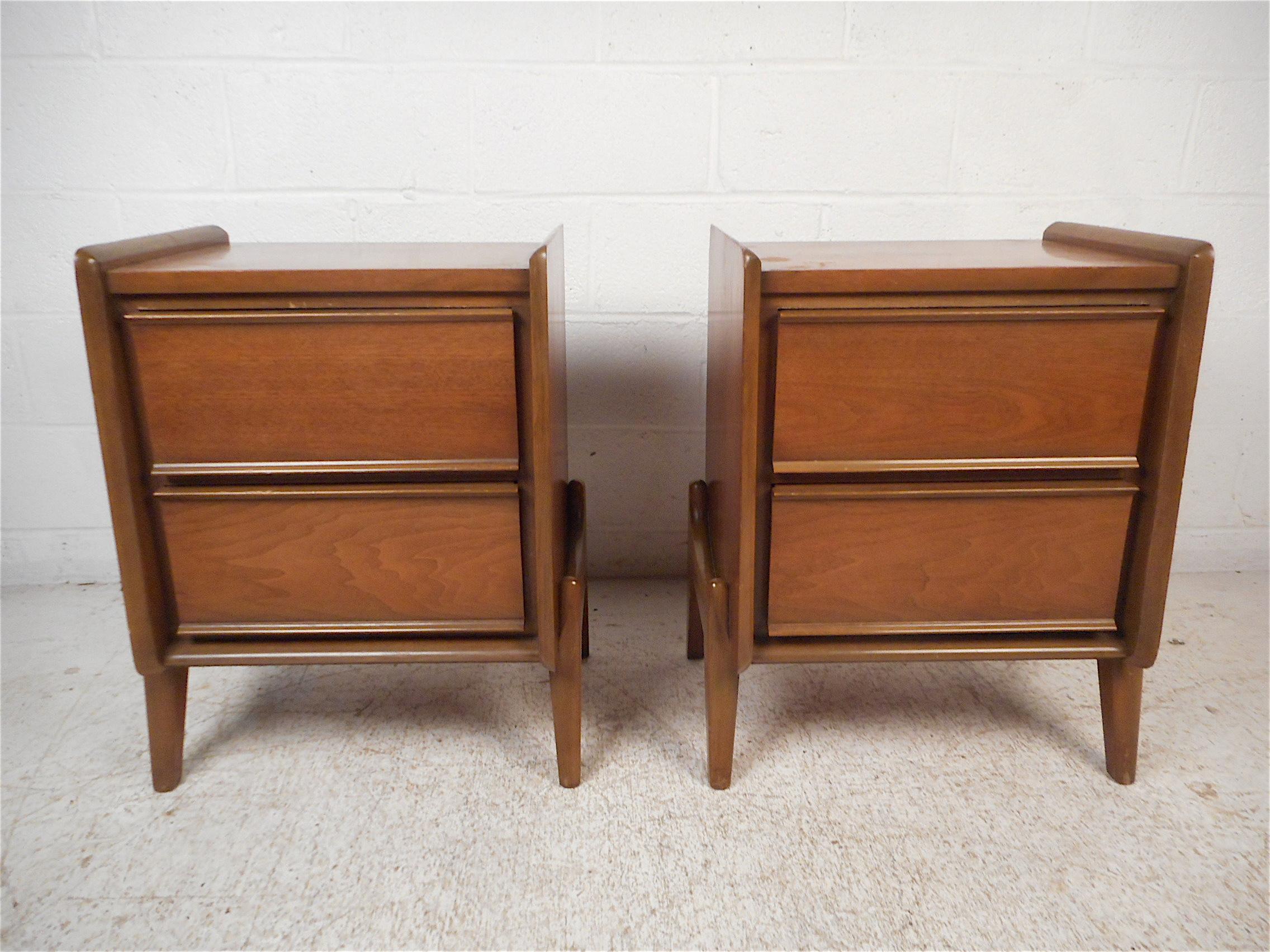 Stylish pair of midcentury nightstands by Grand Rapids Furniture Company. Sleek design with raised edges on the tabletops and sculpted legs. Two spacious drawers on either piece offer ample storage space. This pair is sure to prove a great addition