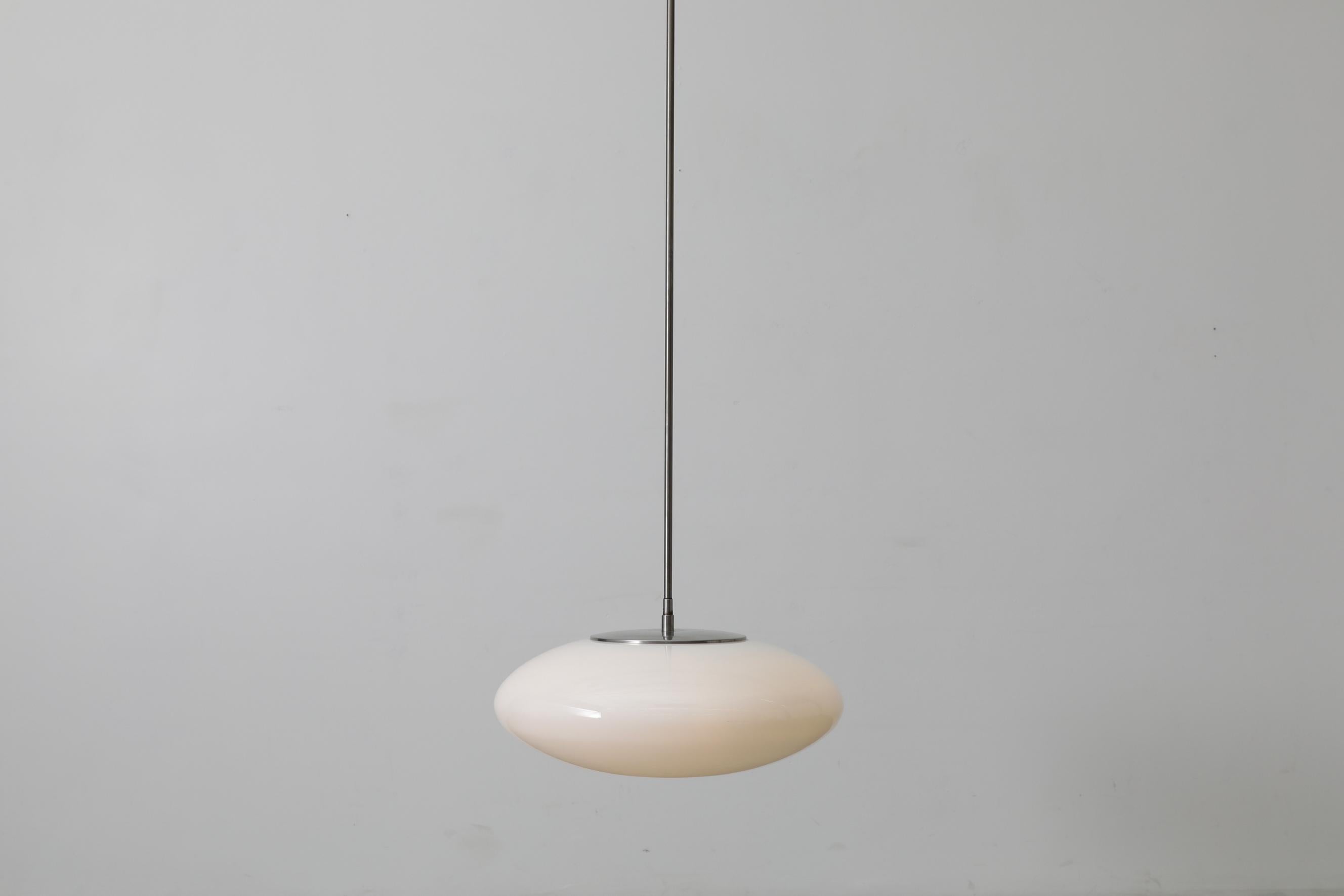 Mid-Century designed milk glass UFO pendants by Nils Jonsson with extra long steel stem and canopy. Giant M&M shaped opaline glass shades, floating at the end of long delicate steel stems. Lights have been converted from fluorescent to incandescent.
