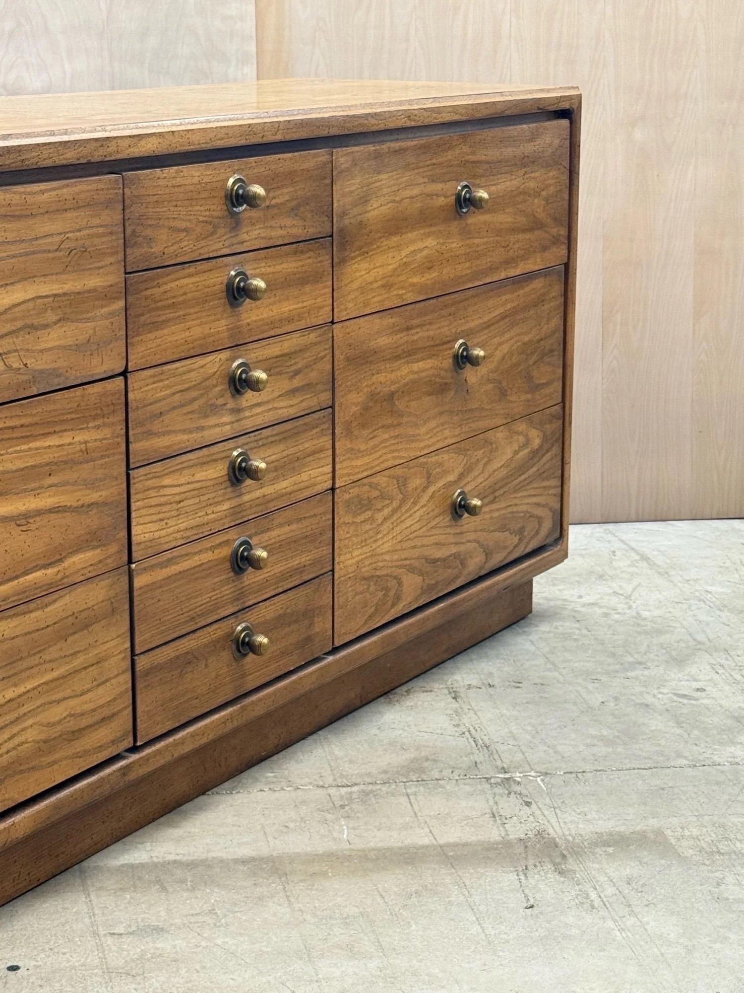Comò a nove cassetti di metà secolo. Questo pezzo è caratterizzato da una splendida venatura del legno e da un'eccellente capacità di stoccaggio. La sezione sinistra e quella destra presentano una serie di tre cassetti profondi. La sezione centrale