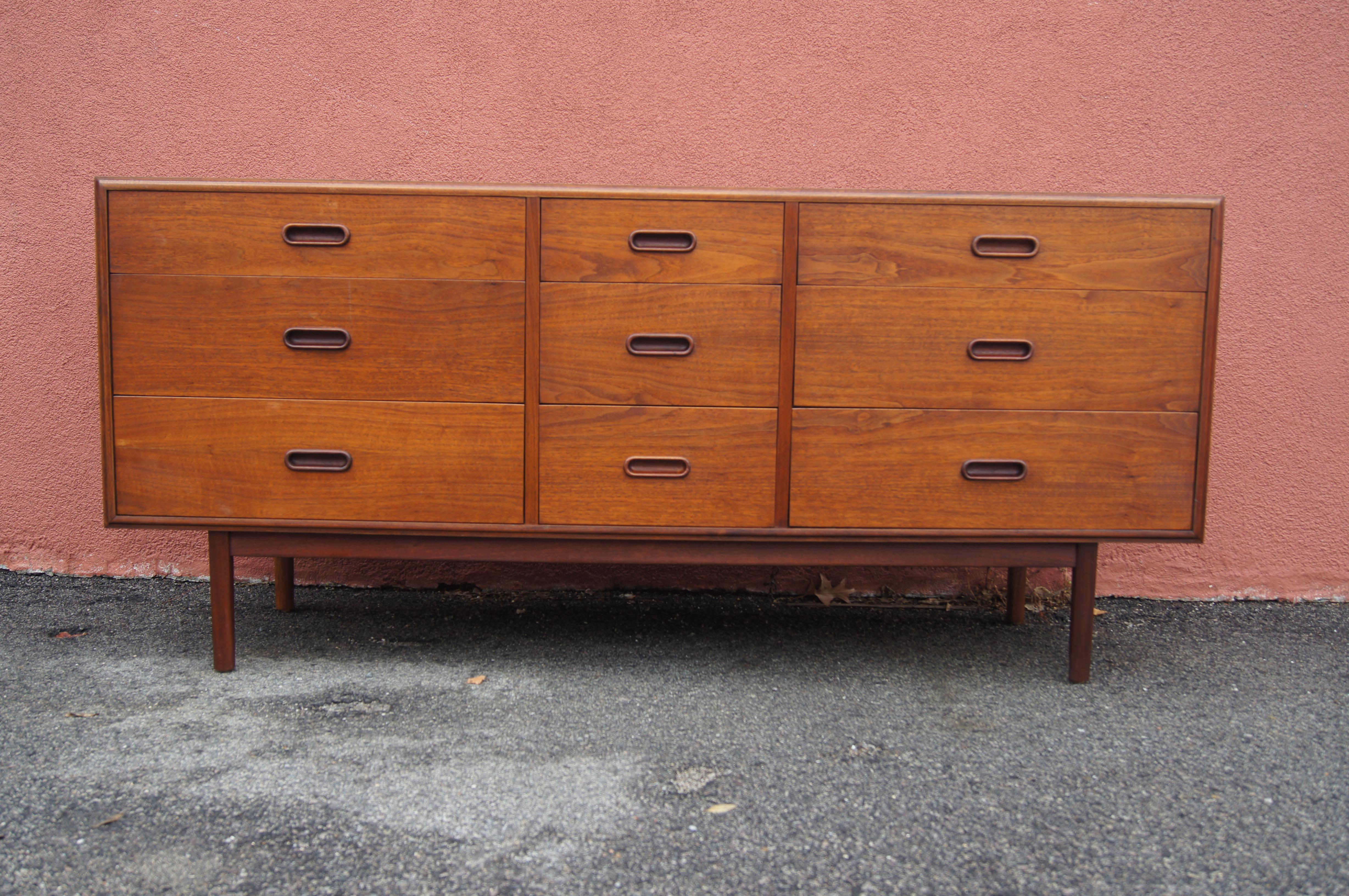 This handsome midcentury dresser features a low teak case of nine drawers, two of which are divided, with a base and frame in a slightly darker stain for contrast. Possibly American in construction, it has oblong wooden handles in the style of Arne