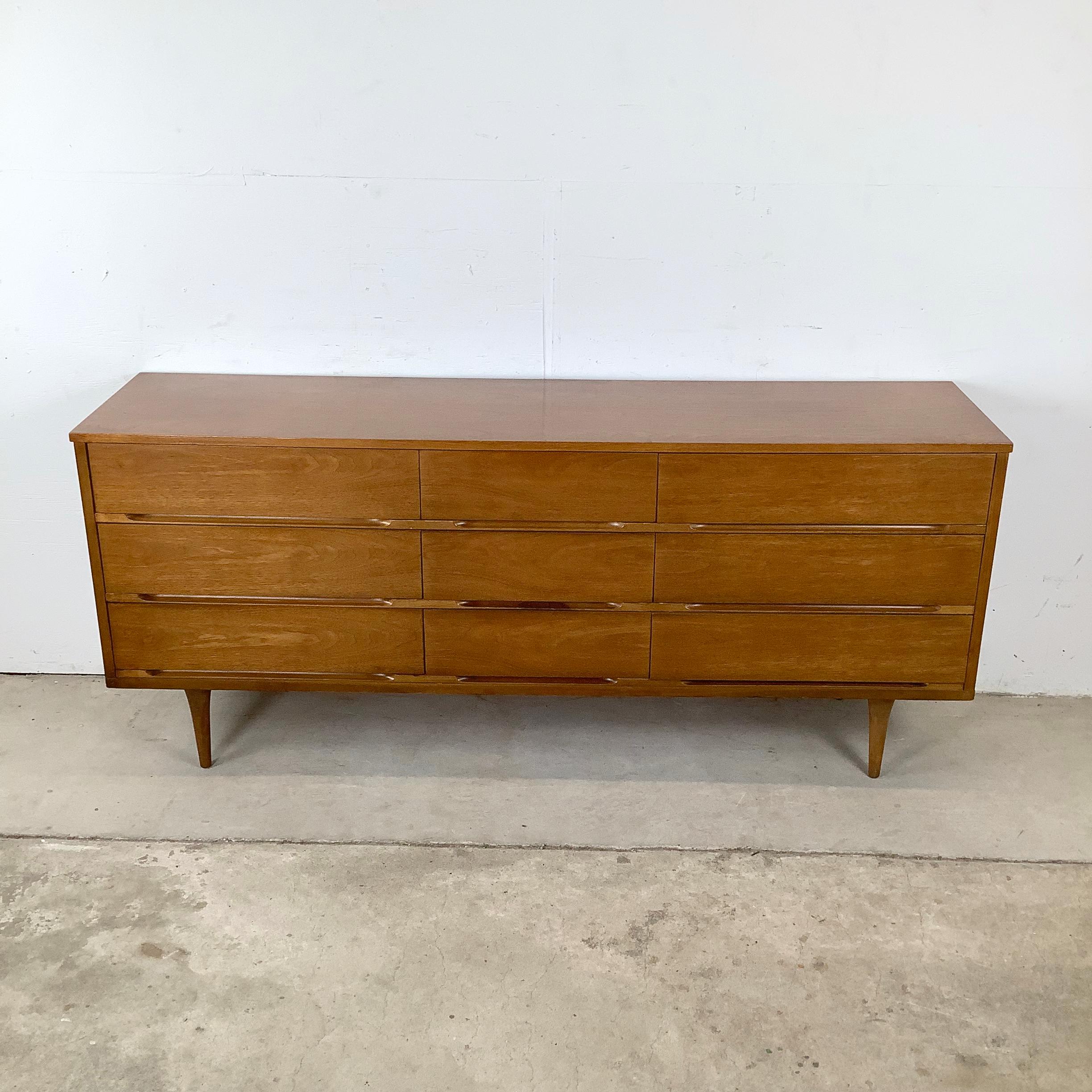 This striking mid-century dresser offers a perfect blend of form and function with its clean walnut case and beautifully sculpted details. The long, low profile is anchored by sleek tapered legs that elevate the piece and give it a light, floating