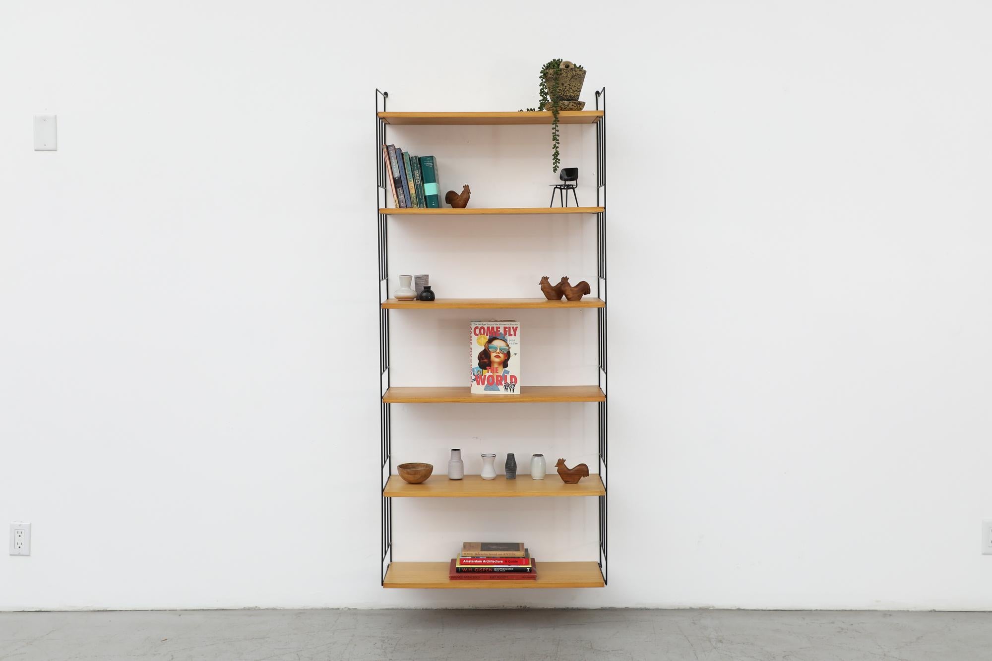 Stunning Mid-Century wall mounted shelving unit with six adjustable light oak shelves on black enameled metal risers. In original condition with visible wear consistent with its age and use.