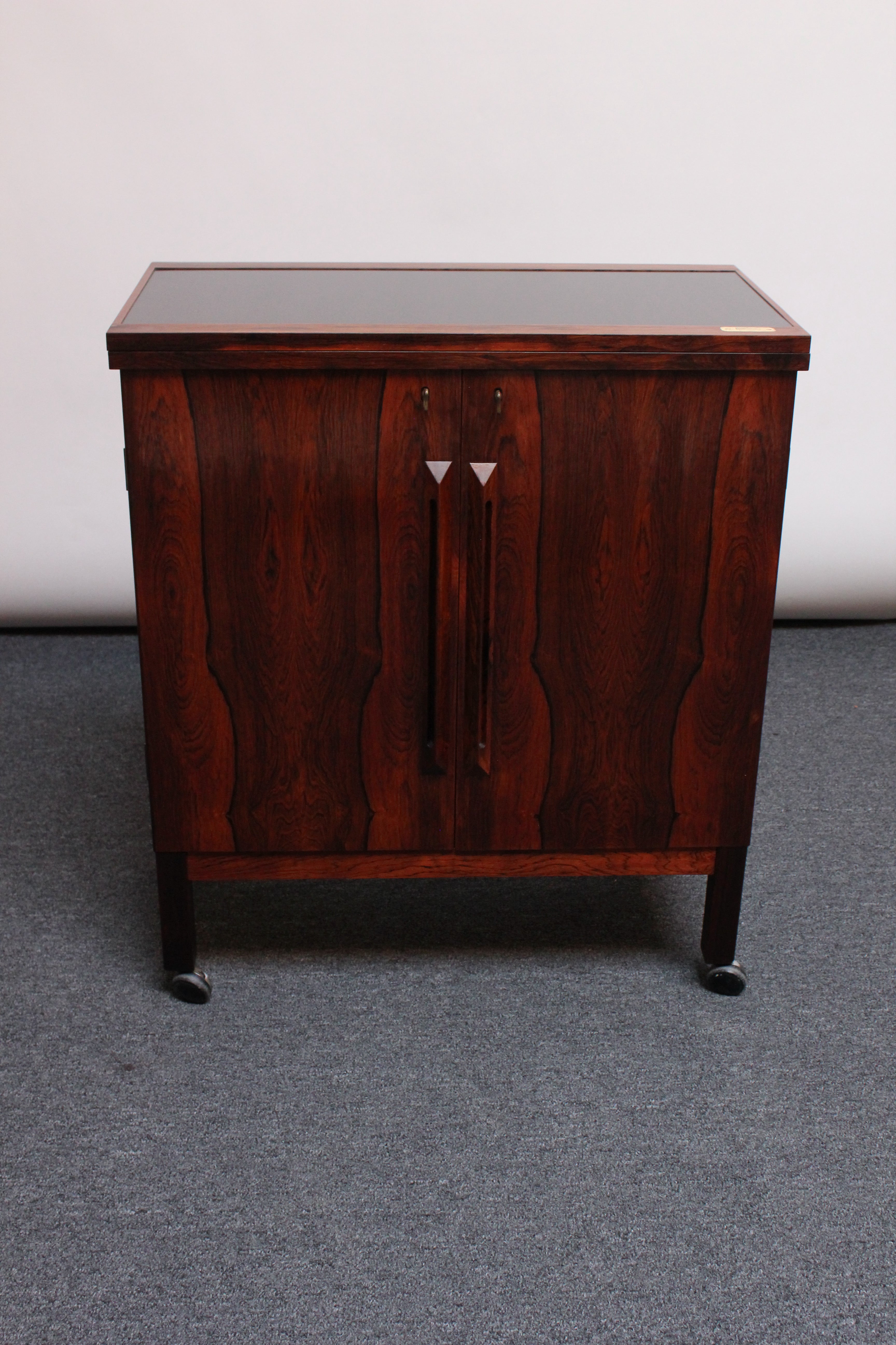 Highly functional and handsome rosewood flip-top bar cabinet on caster wheels with two keys designed by Torbjørn Afdal and produced by Mellemstrands Trevarindustri / Bruksbo of Norway.
The locking cabinet opens to reveal ample storage for bottles