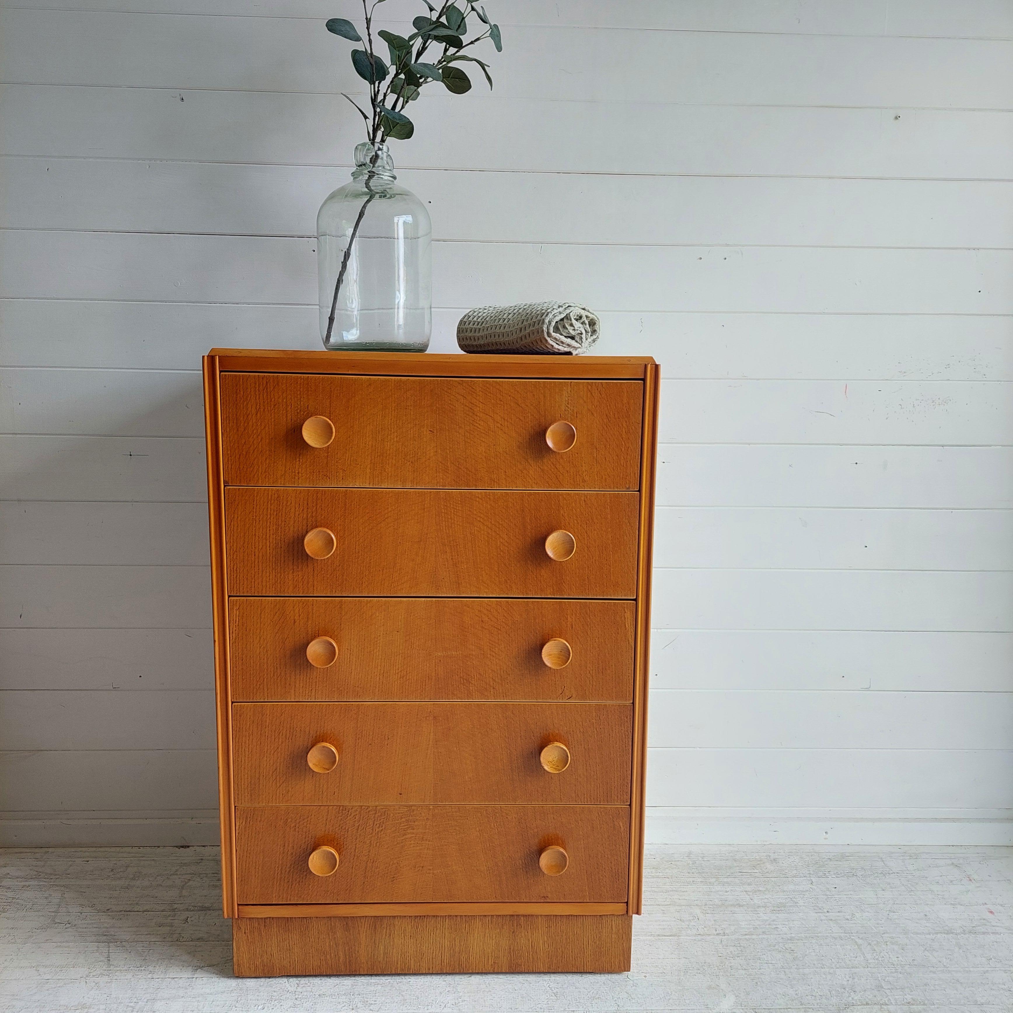 Early 1960s lighter oak chest of five drawers.
Most probably from British makers Meredew, this one possessing unique carved oak knobs. 

It’s a classic mid-century design well executed – simple angles and lines to the oak frame and the five drawers