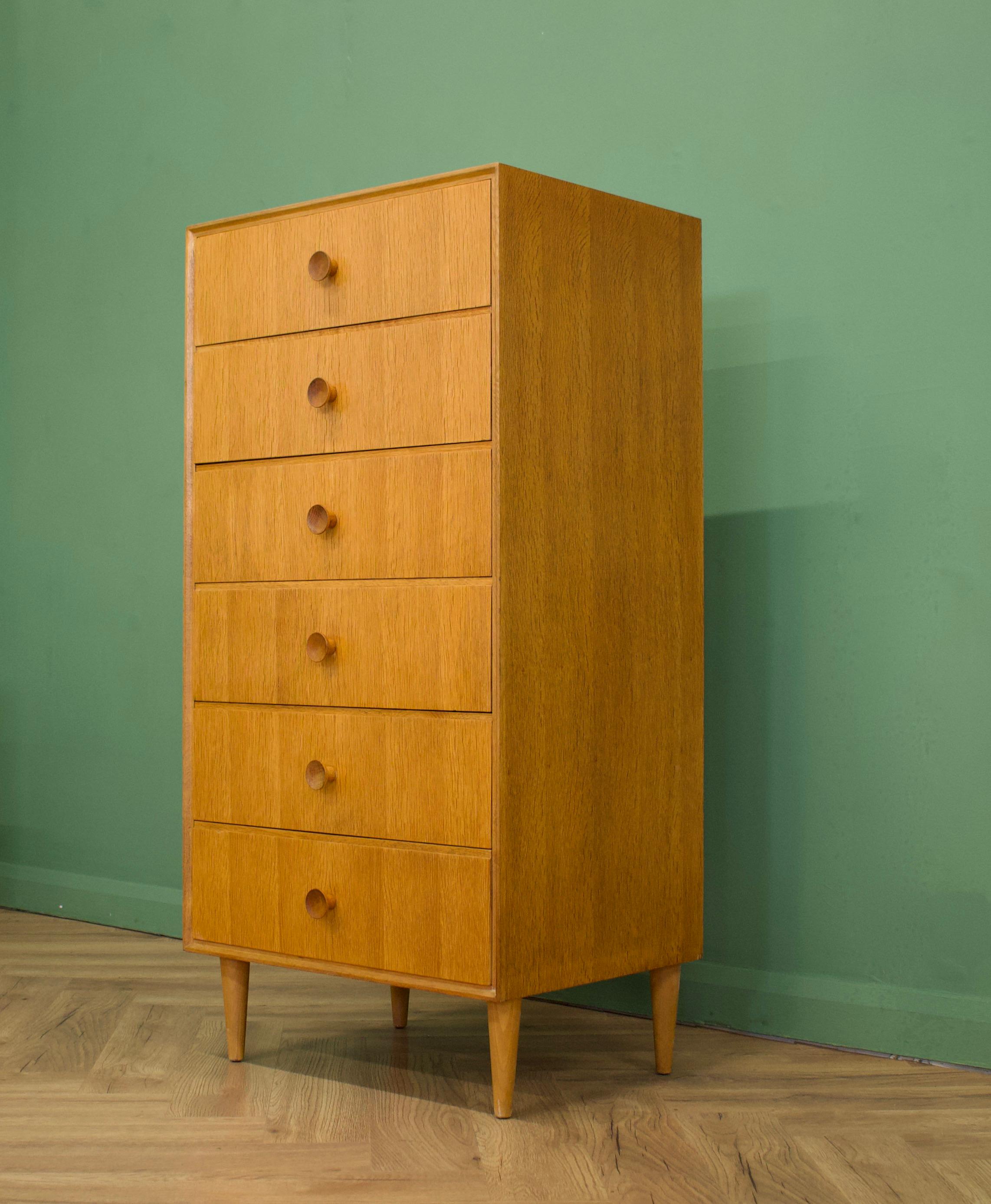 Midcentury tall boy chest of drawers.
Manufactured in the UK by Meredew
Made from oak and oak veneer.

Featuring solid oak handles and six drawers.
 