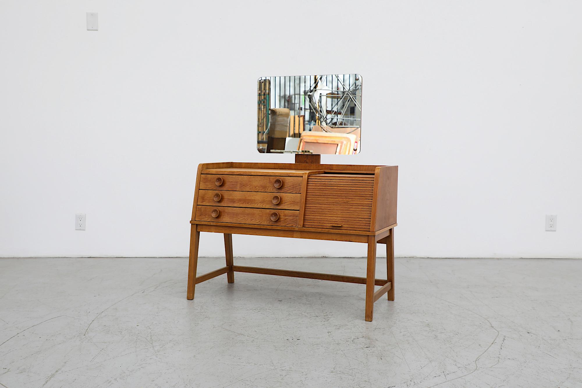 Beautiful Mid-Century oak vanity with tambour door, three drawers and rounded edge mirror. In original condition with visible wear and patina that is consistent with its age and use.