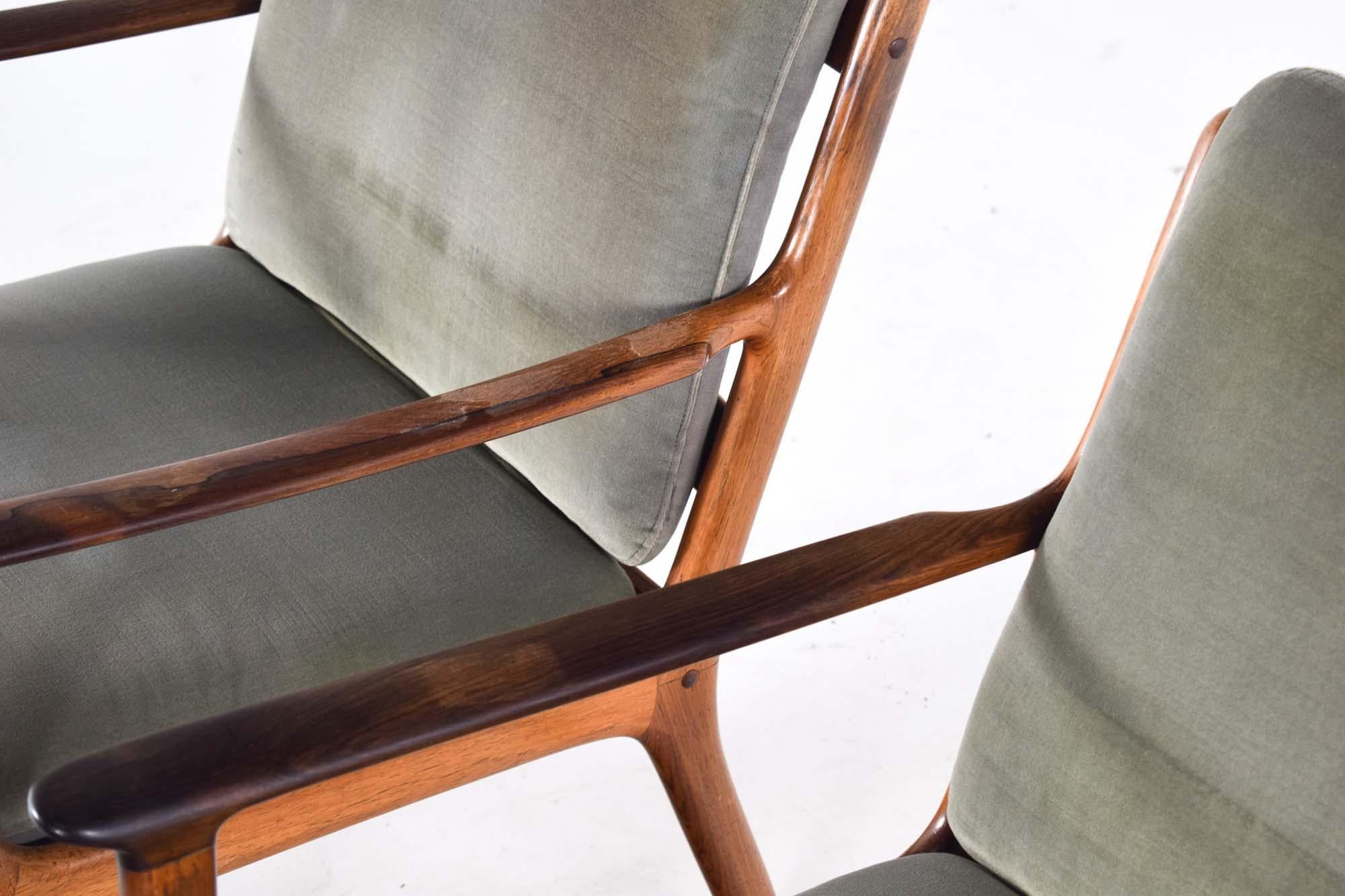 Dieses exquisite Paar Sessel aus der Mitte des Jahrhunderts, entworfen von Ole Wanscher für die Poul Jeppesen Møbelfabrik, Modell PJ112, ist ein Meisterwerk dänischen Designs. Die aus glänzendem Palisanderholz gefertigten Stühle zeigen die satten,