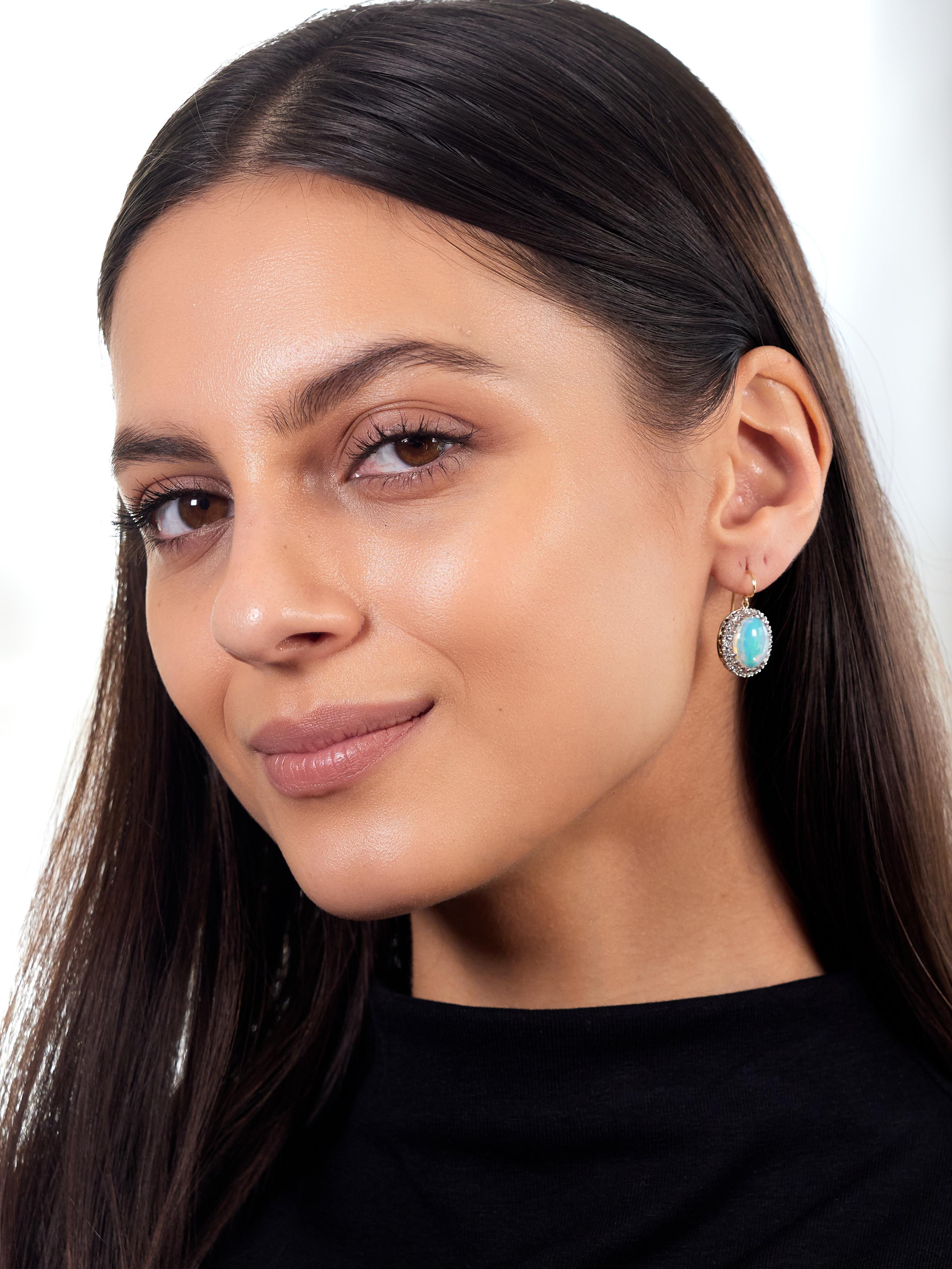 Centering oval shaped opal cabochons measuring 10.0 x 12.0 mm
White in body color and displaying a spectral play-of-color
Set with white gold prongs with a recessed halo surround
Single cut diamonds weigh approximately 0.40 carat total
Eye clean and