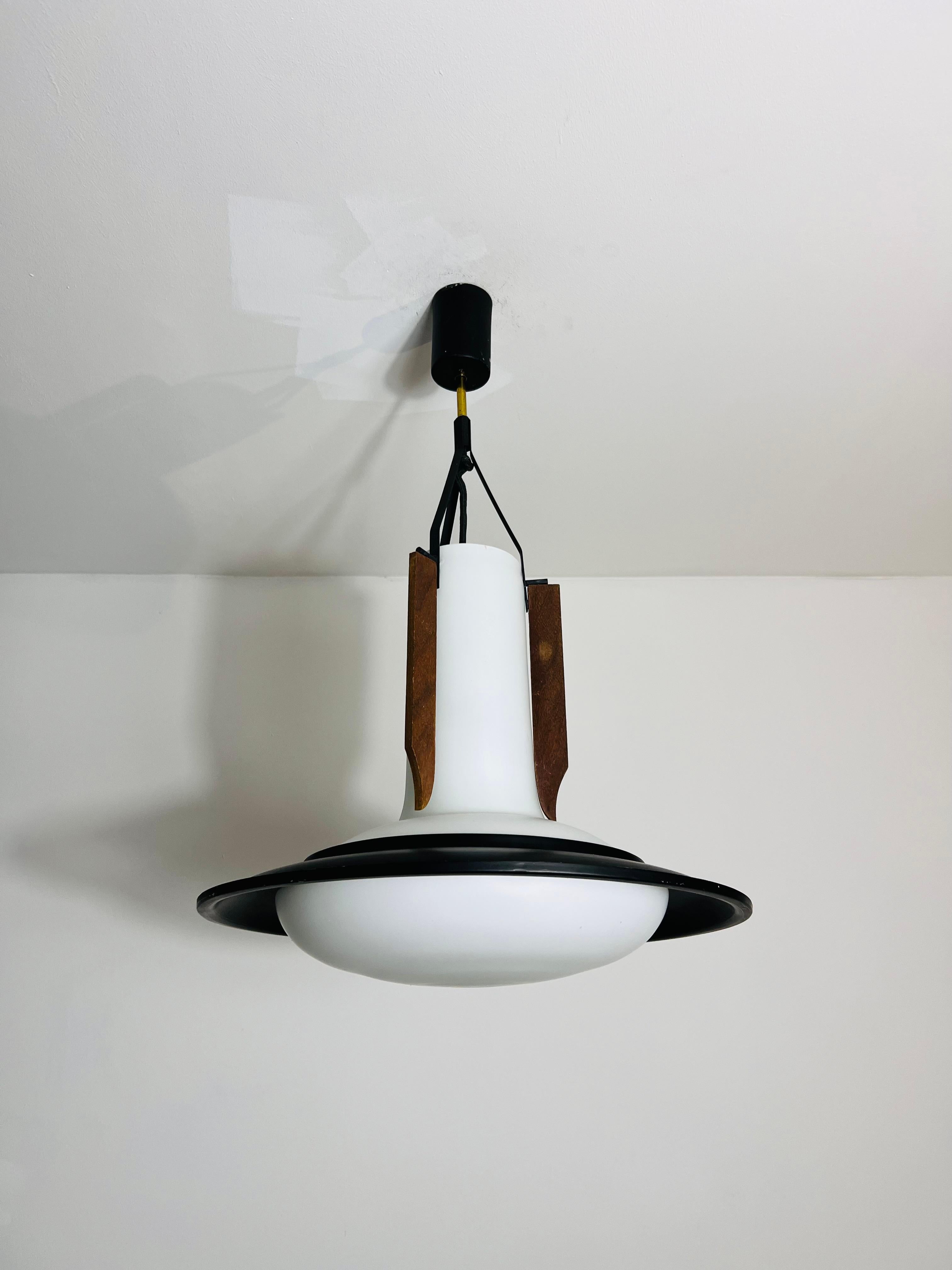 Questa elegante lampada da soffitto italiana degli anni '60 è uno splendido esempio di design moderno di metà secolo. Il centro è costituito da un paralume in vetro opalino di ottima fattura, accentuato da un elegante anello in metallo nero che