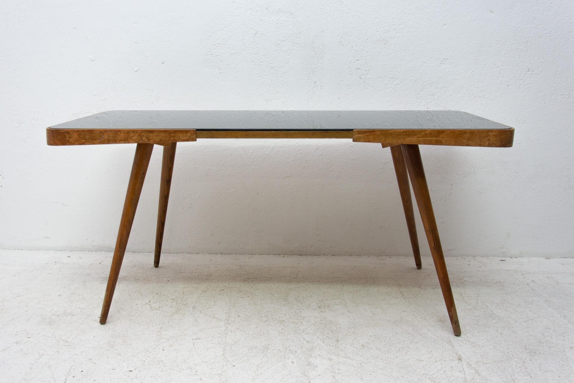 Midcentury opaxite glass coffee table from the 1960s. Associated with the world-renowned exhibition EXPO 58 in Brussels. It was produced by “Ceský nábytek n.p.”. It features a beechwood structure and a black glass tabletop. In very good vintage