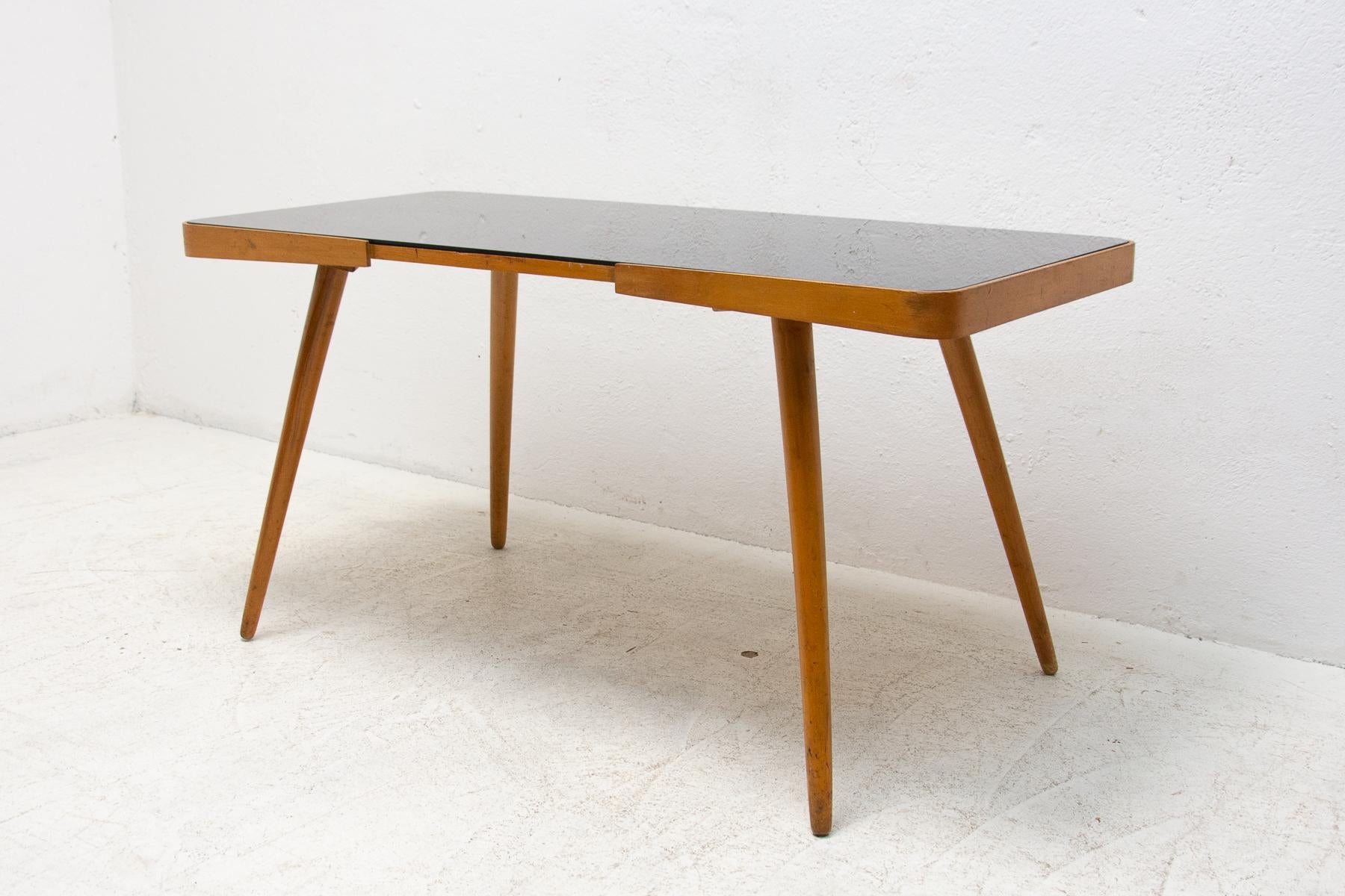 Mid-century opaxite glass coffee table from the 1960's. Associated with the world-renowned exhibition EXPO 58 in Brussels. It was produced by “Ceský nábytek”. It features a beechwood structure and a black glass tabletop. In very good Vintage