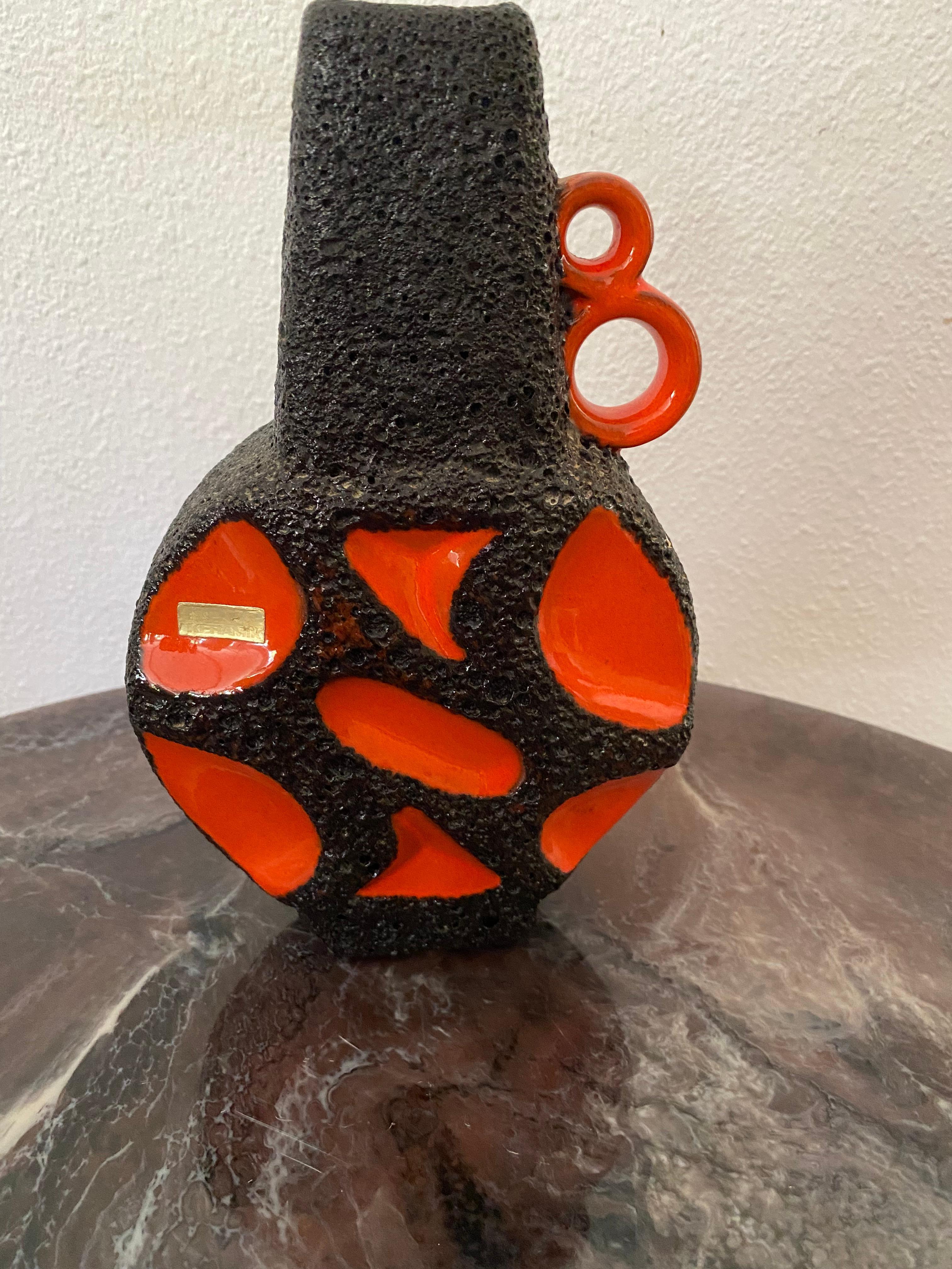 Un vase Roth Keramik, aux contours orange avec de la lave noire. Ces vases sont très recherchés. Le modèle est également appelé le Banjo, en raison de sa forme.
L'autocollant/l'étiquette d'origine est présent.

