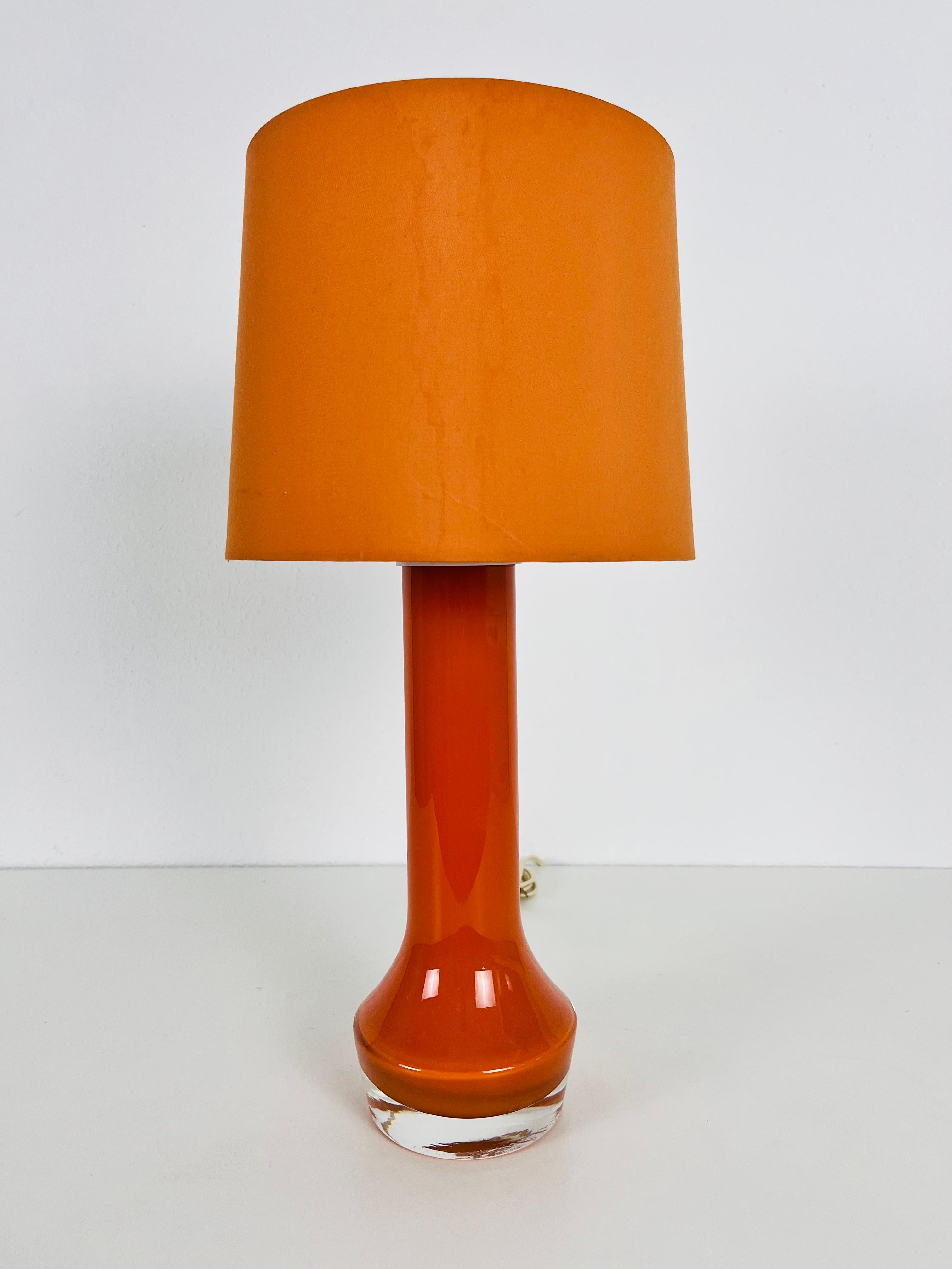 A beautiful large table lamp made in the 1960s. The base is made of heavy orange colored glass. The lamp shade is made of fabric and has a dark orange color.

The light requires one E27 light bulb. Works with both 120/220 V. Good vintage
