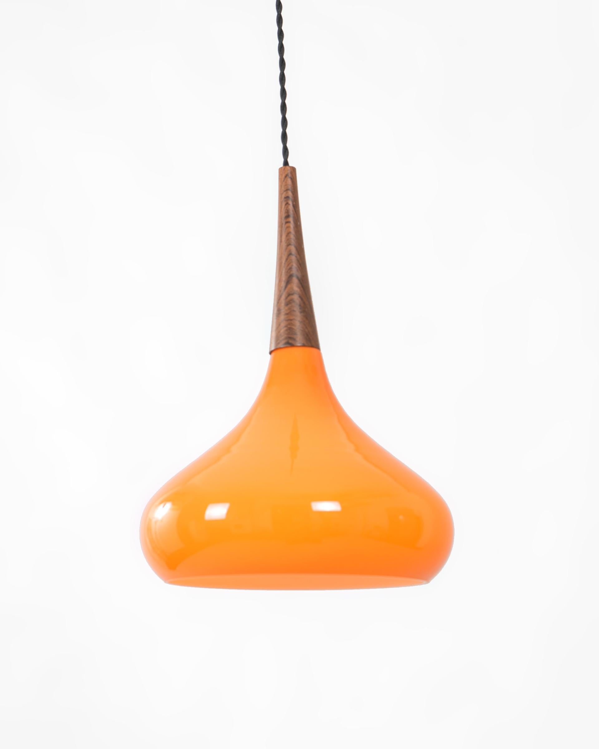 Lámpara de techo mid-century de cristal naranja con aplique en madera de teca. El cable original ha sido sustituido por un cable trenzado de cuerda de algodón negro.

