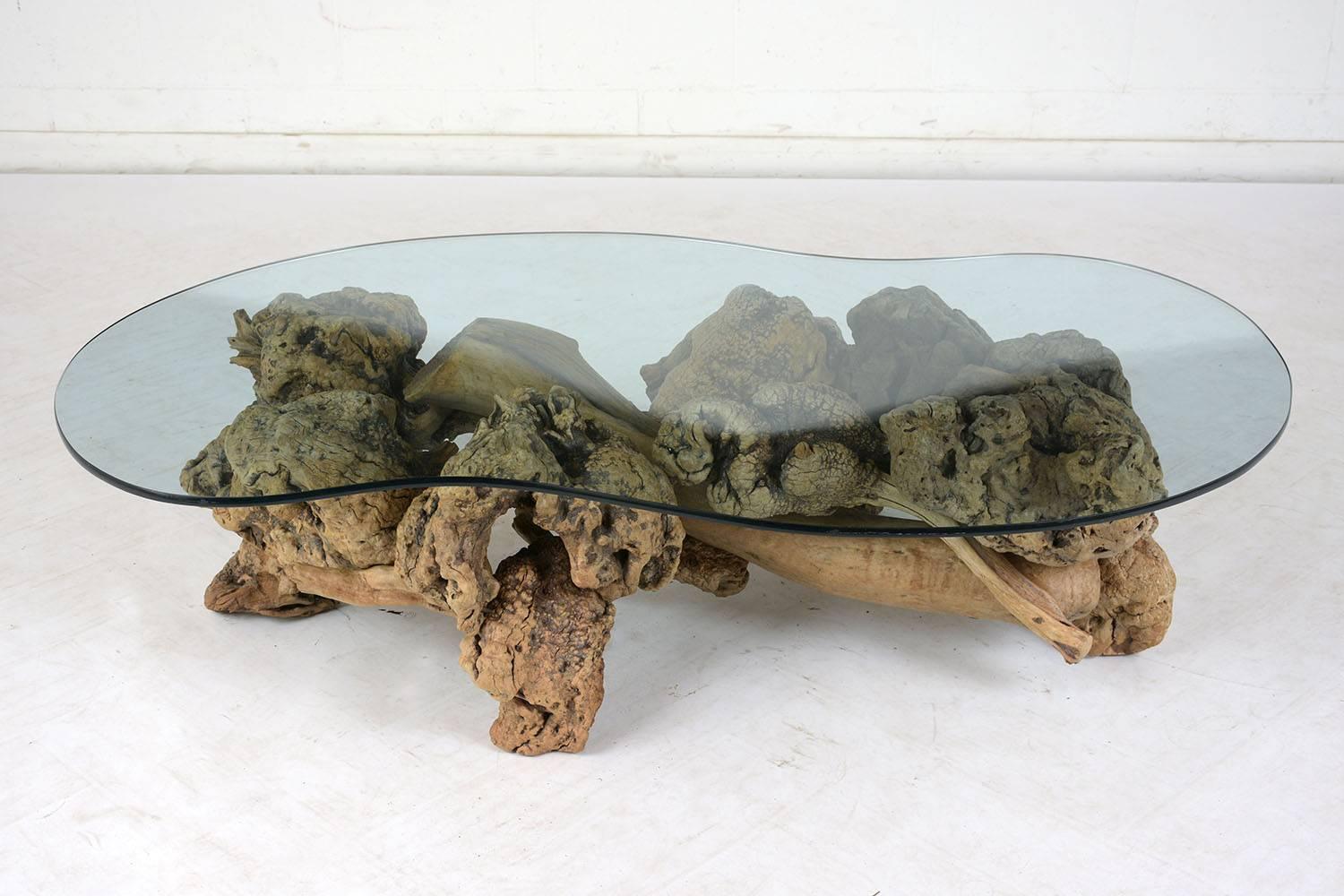 This 1960s mid century coffee table features a stunning organic form tree root as its base. The natural stained tree root has many different textures with both knotted and smooth sections and dates to the early 1900s. The kidney-shaped glass top is