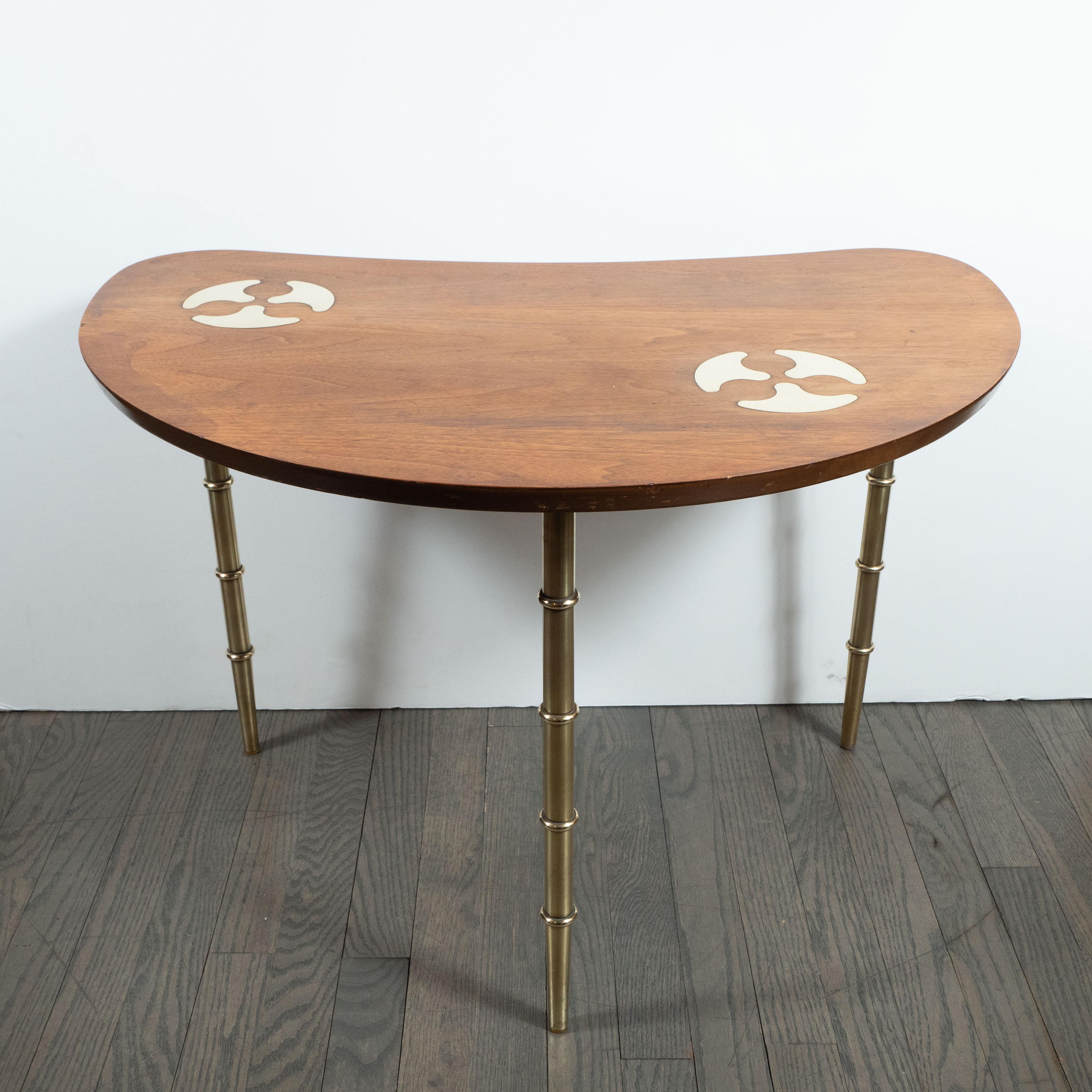 This refined Mid-Century Modern table was realized by the celebrated 20th century design firm, Mastercraft, in the United States, circa 1970. It features an amorphic bowfront top in hand rubbed walnut with a pair of brass inlays consisting of three