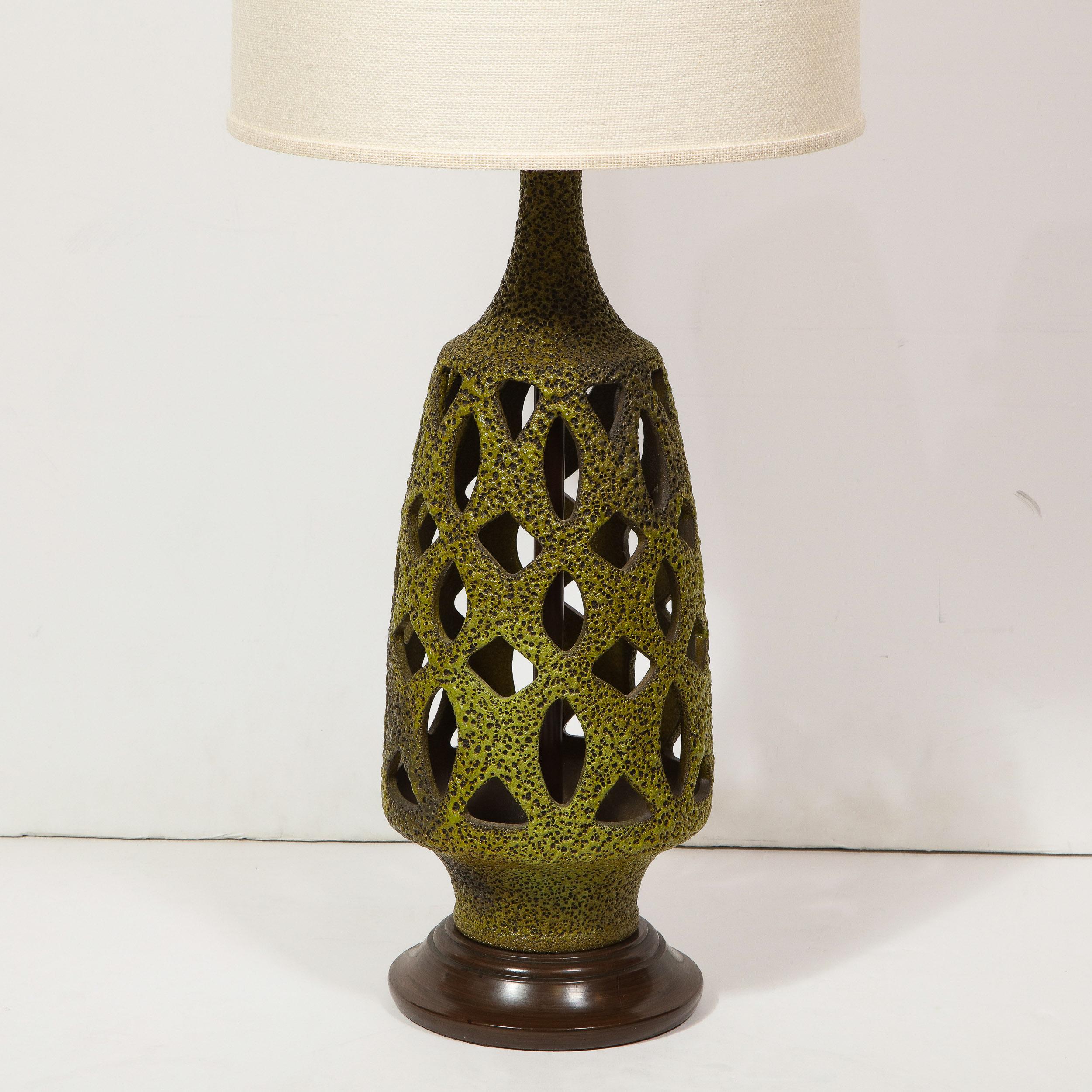 This stunning and sophisticated Mid-Century Modern table lamp was realized in the United States circa 1960. Sitting on a subtly convex painted metal base, the lamp flares out into a gently tapering conical body and elegant hourglass form neck. Its