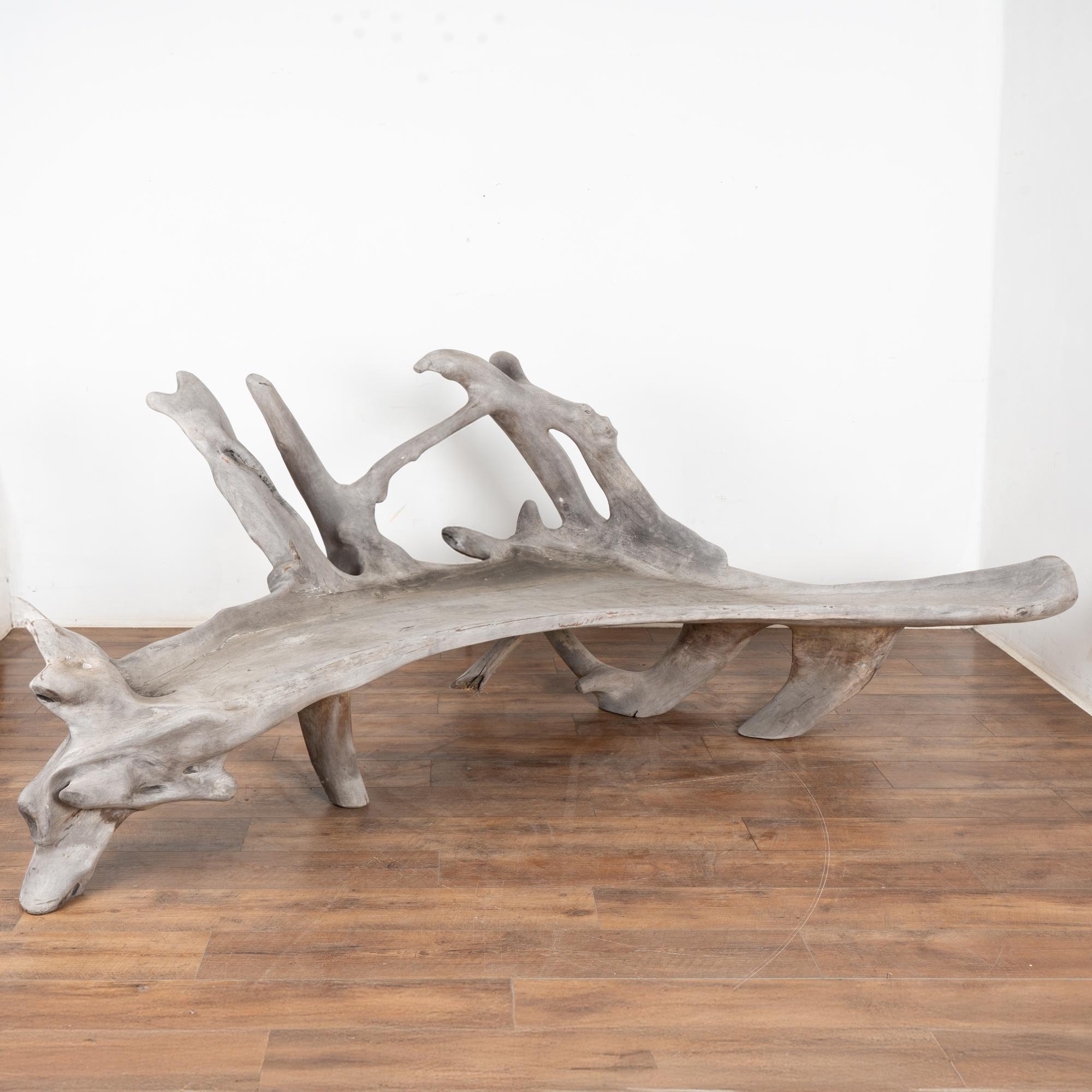 The organic appeal of this teak root bench draws one to it in fascination. Worn and weathered through the elements, the seat and back are all one solid piece of wood; at over 9' wide it is naturally gnarled and twisted.
While it serves well as an