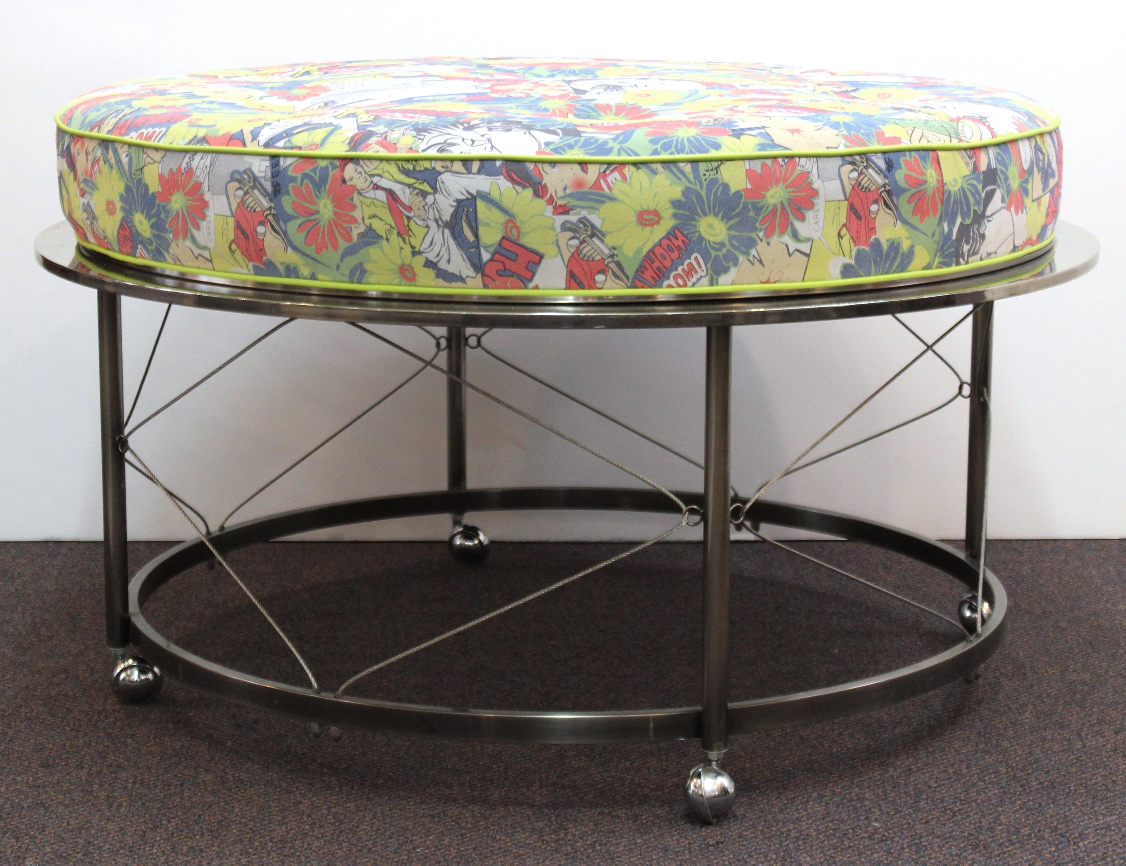 Midcentury ottoman with chrome frame on castors and new upholstery. Features include a circular frame with wire trestles and colorful comic book inspired upholstery. Wear appropriate to age and use. The ottoman remains in very good condition.