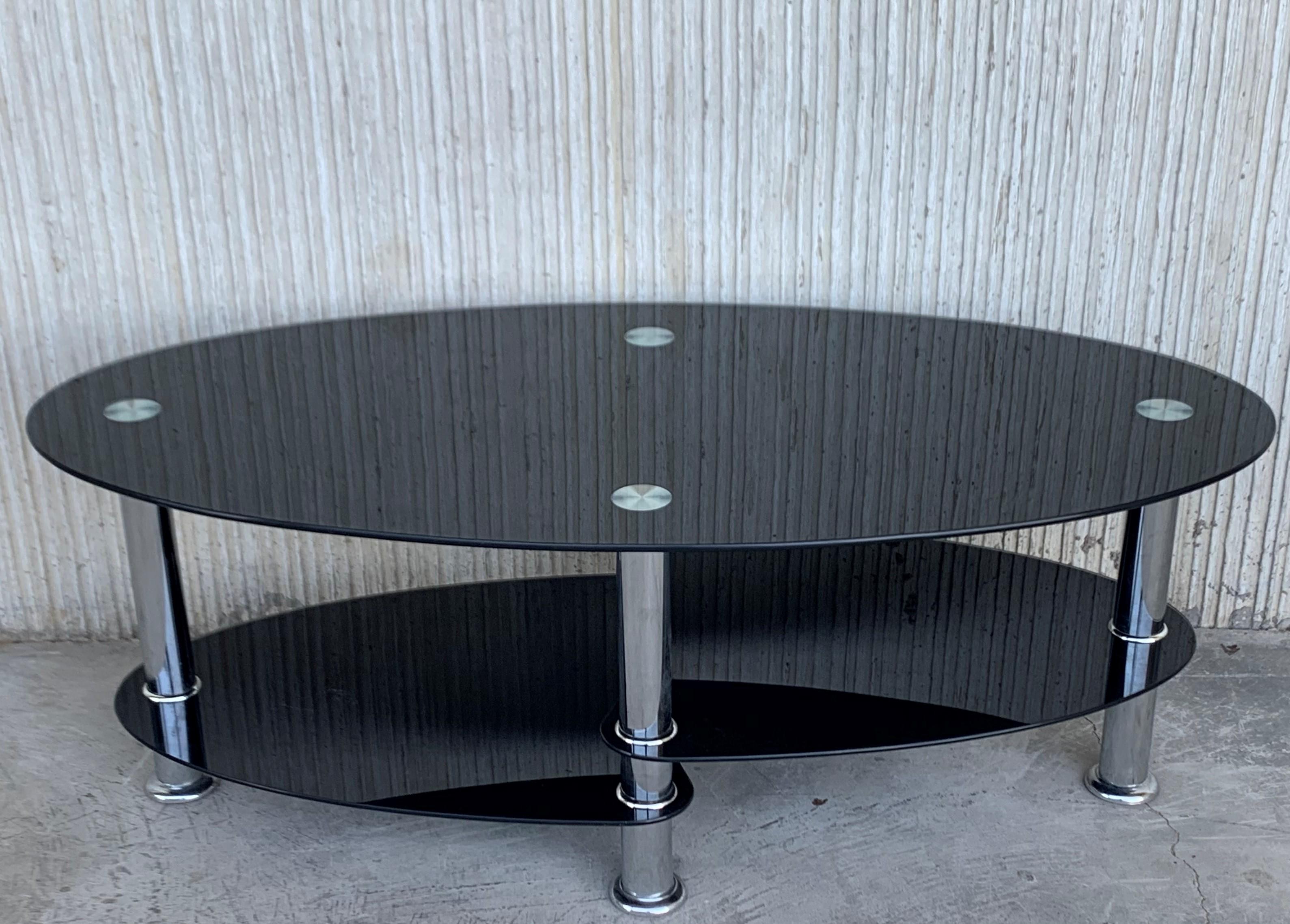 Midcentury oval Art Deco center table in black glass tops and chrome

It has two shelves in different heights:
Measures: Total height: 17.32in
Medium shelve: 7.48in
Low shelve: 4.92in.