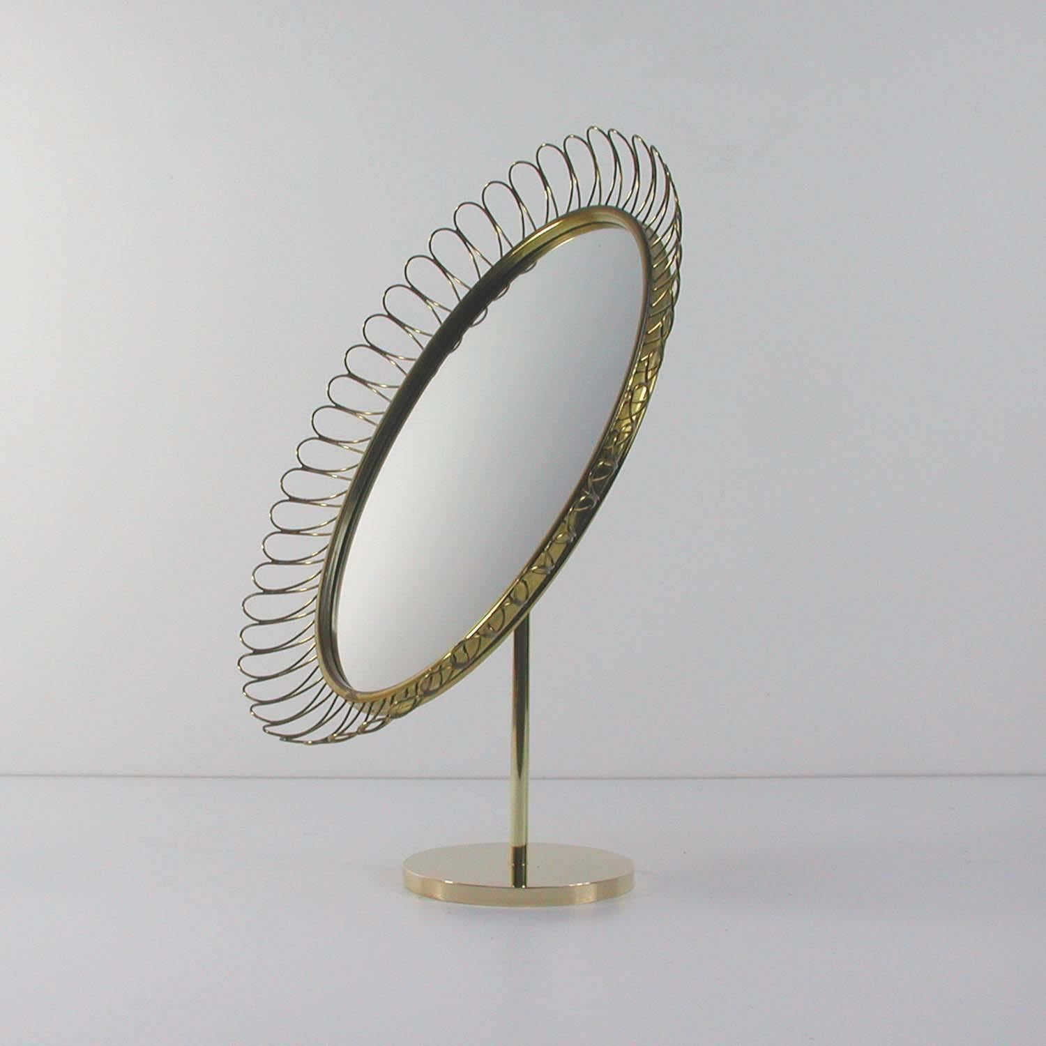 This oval vanity mirror was made in Sweden in the 1950s in the manner of Josef Frank for Svenskt Tenn. It is made of a brass looped frame and has got a solid brass foot. The rear is made of teak veneer. The mirror is adjustable.