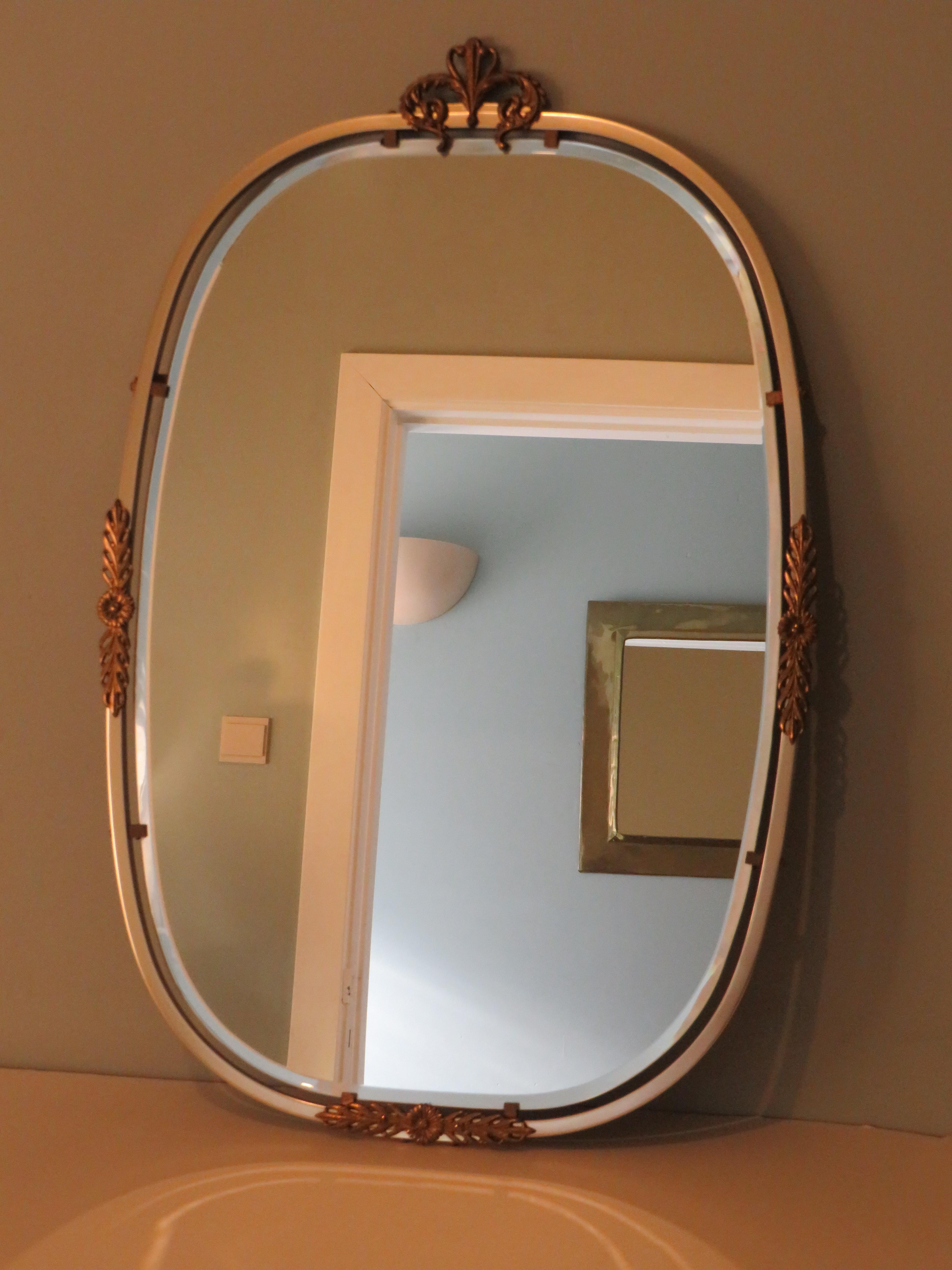 The mirror has a polished edge and is held by means of metal clips in a nickel-plated metal edge, which is decorated with brass ornaments. On both sides and at the bottom is a flower ornament and at the top a heart-shaped decoration.
The mirror is