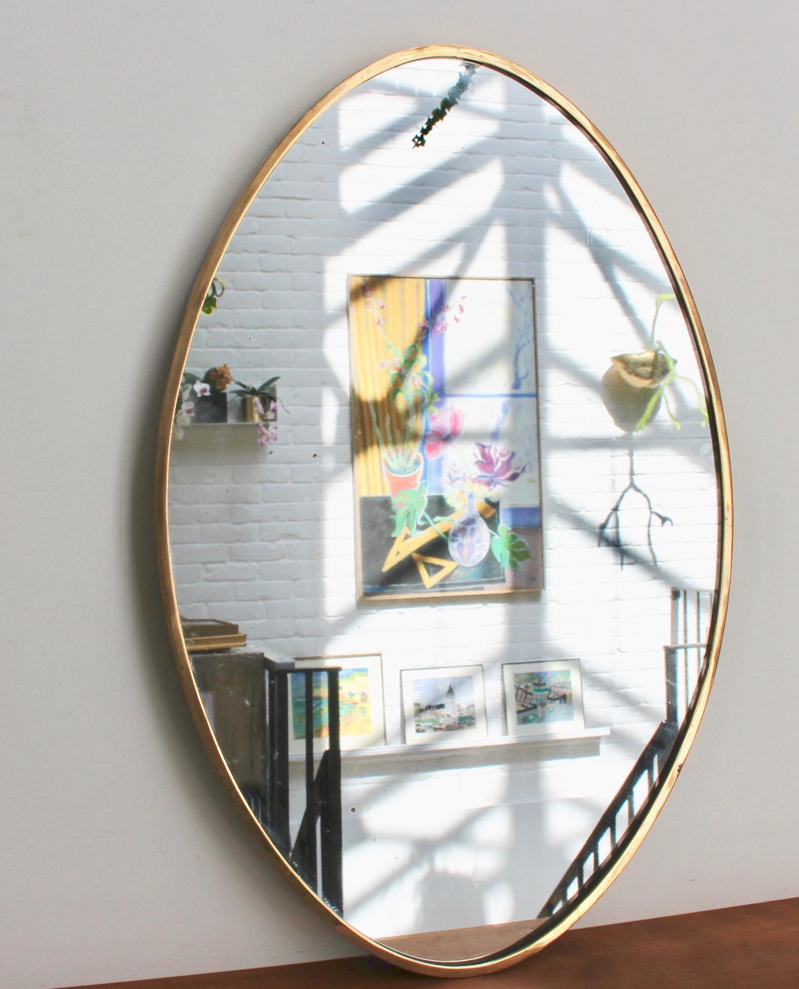 Midcentury Italian oval wall mirror with brass frame (circa 1950s). The mirror is oval in shape and very smart with irresistible durability. The visual impression is elegant and very distinctive in a modern Gio Ponti style. The mirror is in fair