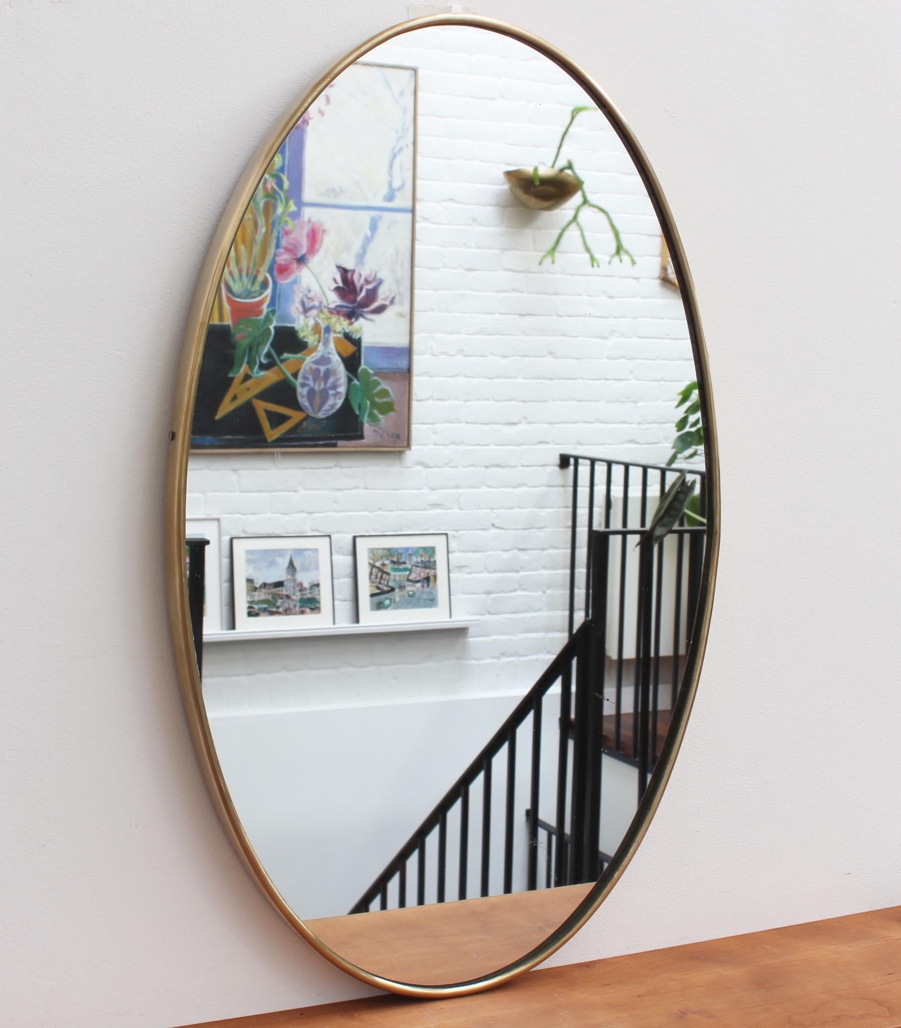 Midcentury Italian wall mirror with brass frame (circa 1950s). The mirror is sensuously oval-shaped and both classically elegant and distinctive in a modern Gio Ponti style. The piece is in good vintage condition with some evident but characterful