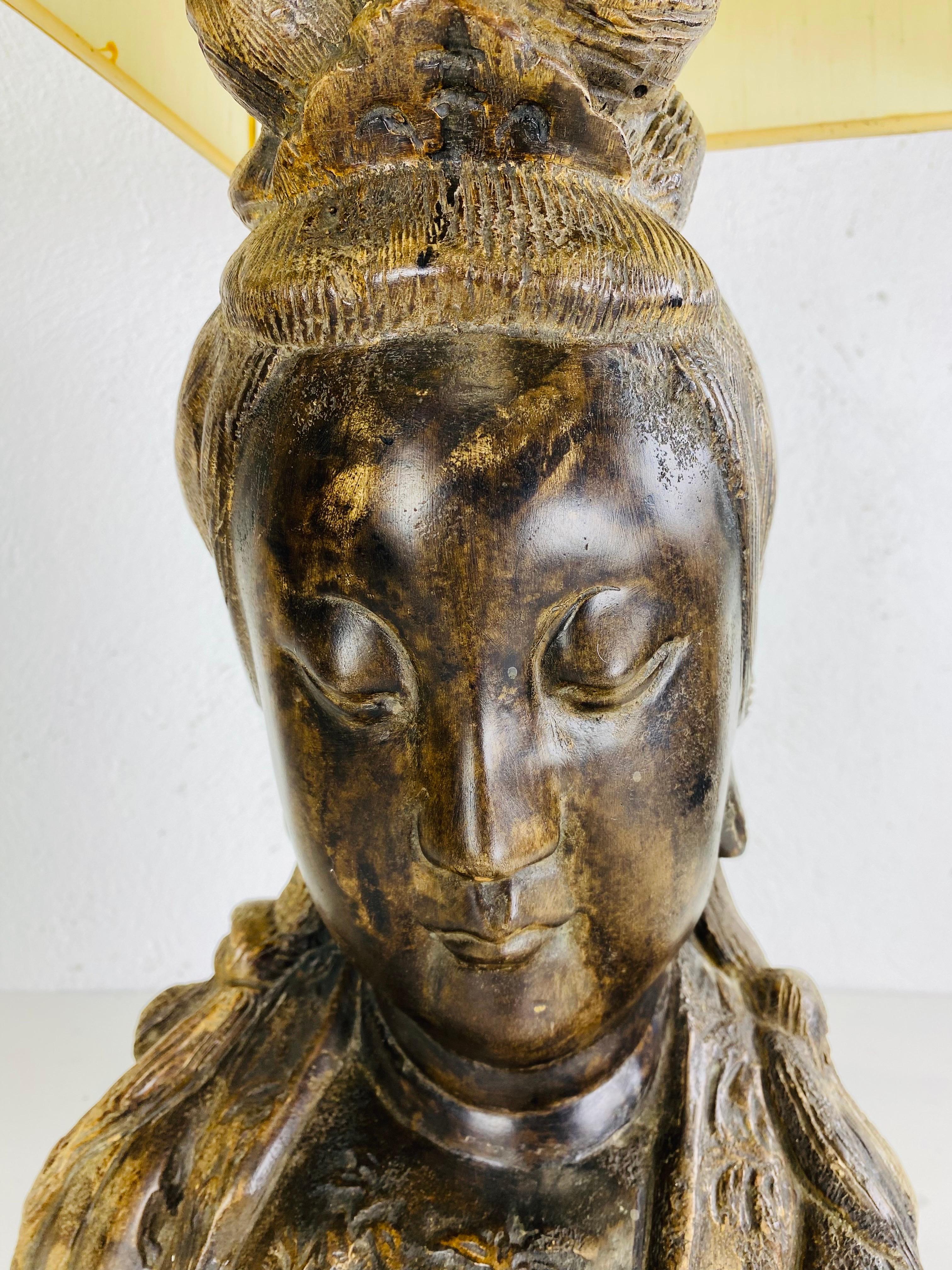 This is an oversized mid-century vintage Asian style lamp. This lamp is a bust of Guan yin and features is original large silk shade. The bust has a patinated bronze finish to the surface and is mounted on a black base. The lamp is in the style of