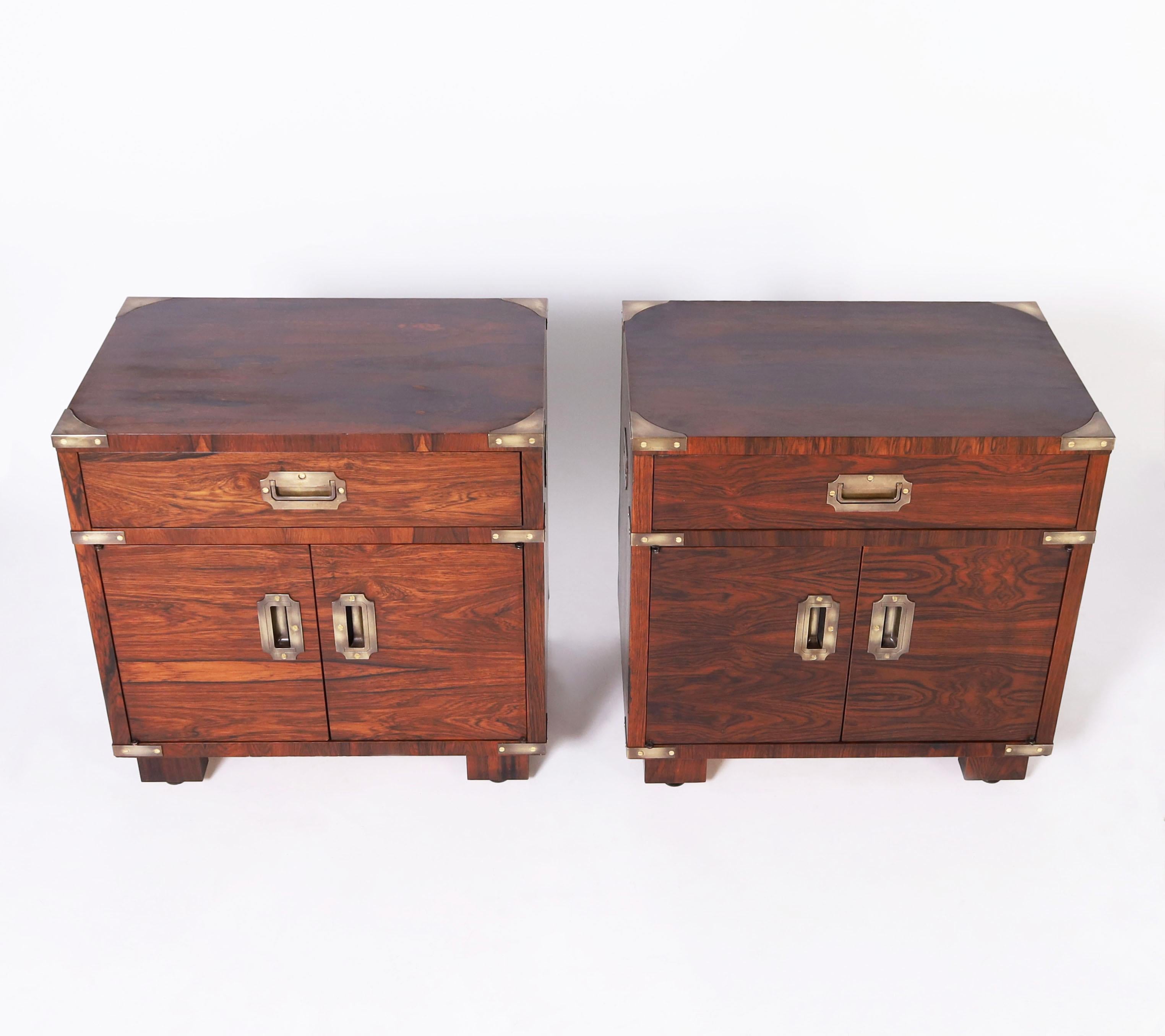 Chic pair of vintage campaign style stands crafted in dramatic grained rosewood with a drawer and two doors each, burnished brass hardware and simple block feet. Perfect marriage of modern and traditional design.