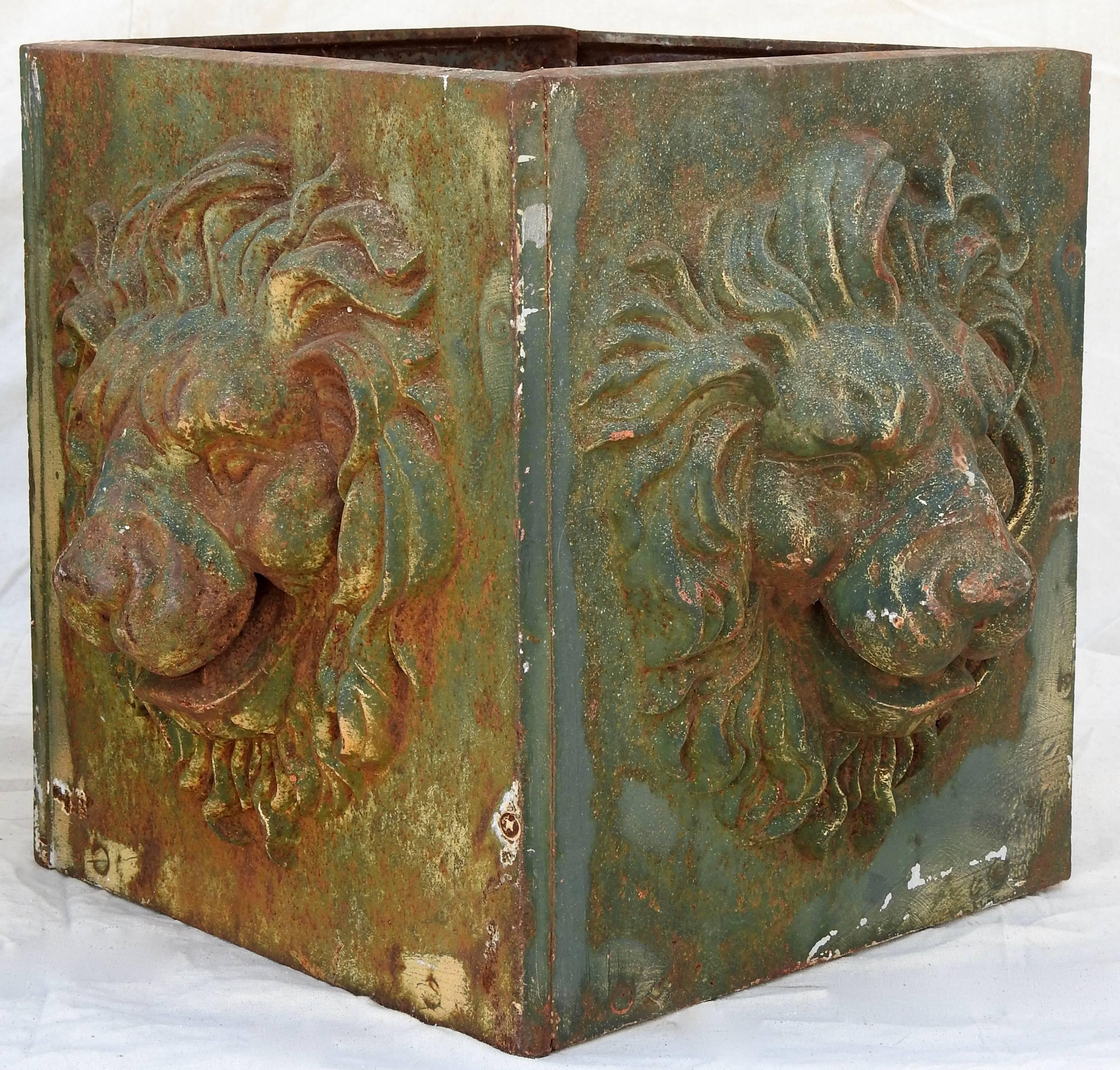Featured is an exceptional pair of cast iron planter boxes. This pair of boxes have a dimensional lions face on each side. They are in the shape of a square box and have a greenish color with a rusty patina.