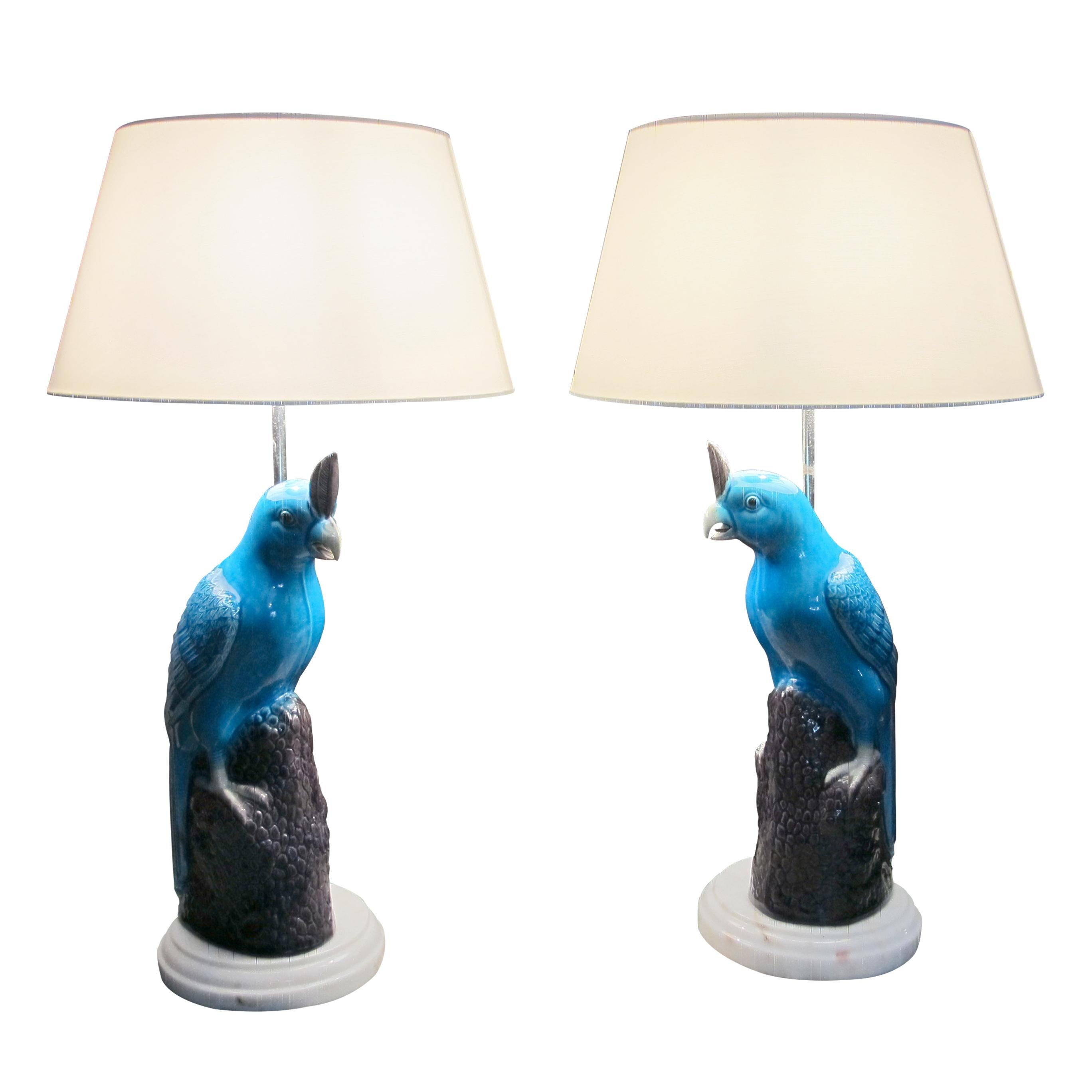 Pareja de lámparas de mesa loro de cerámica esmaltada, inspiradas en los diseños asiáticos de mediados de siglo y fabricadas en Italia. Los loros están representados con un llamativo vidriado azul, posados sobre bases oscuras y texturadas que