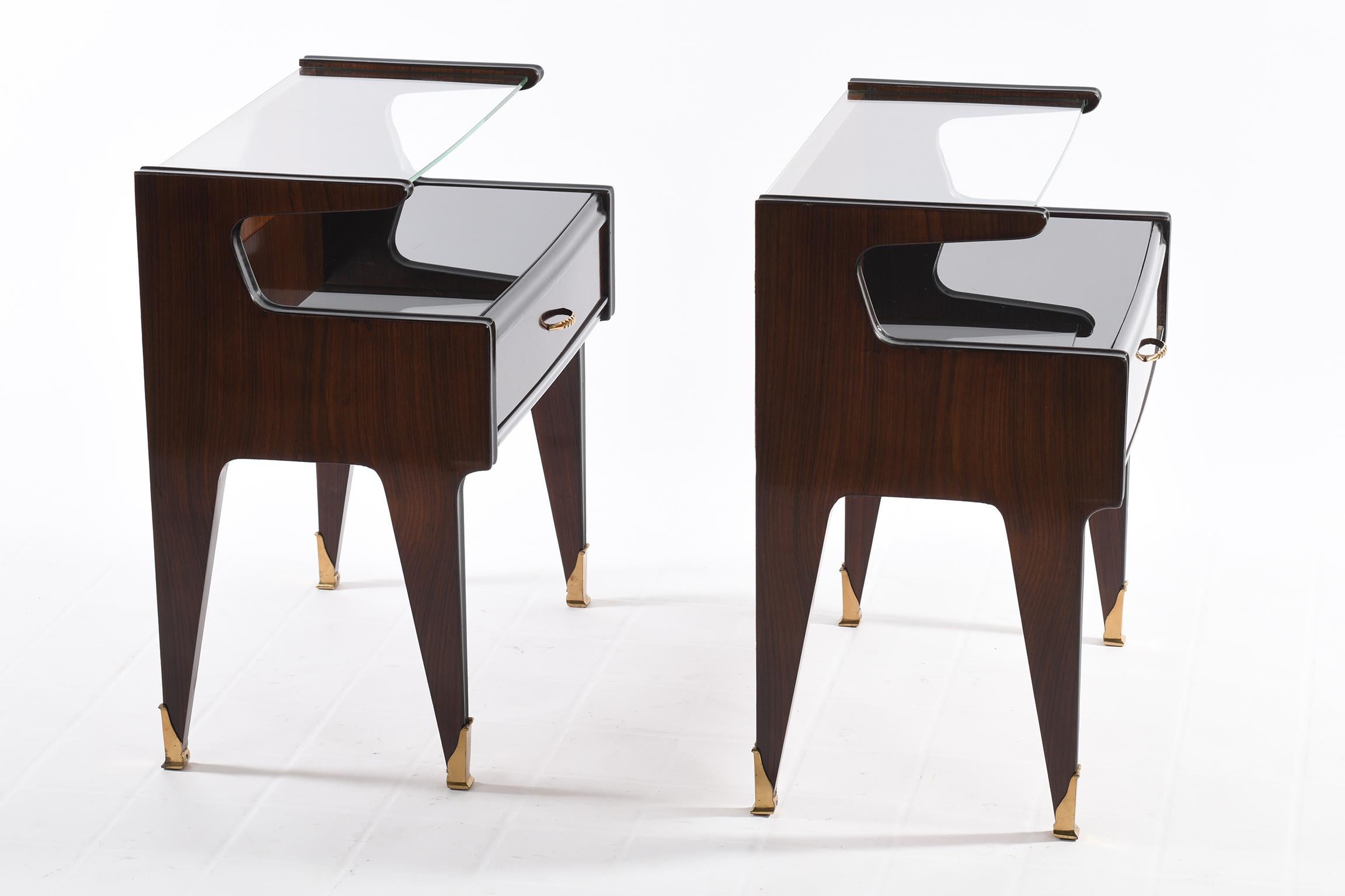 Pair of Italian bedside tables with double top, the lower one in black glass, the upper one in transparent glass, has a drawer with precious wood arranged in a herringbone pattern.
Handle and feet in cast brass.
 Dassi Manufacture Italy 1950's