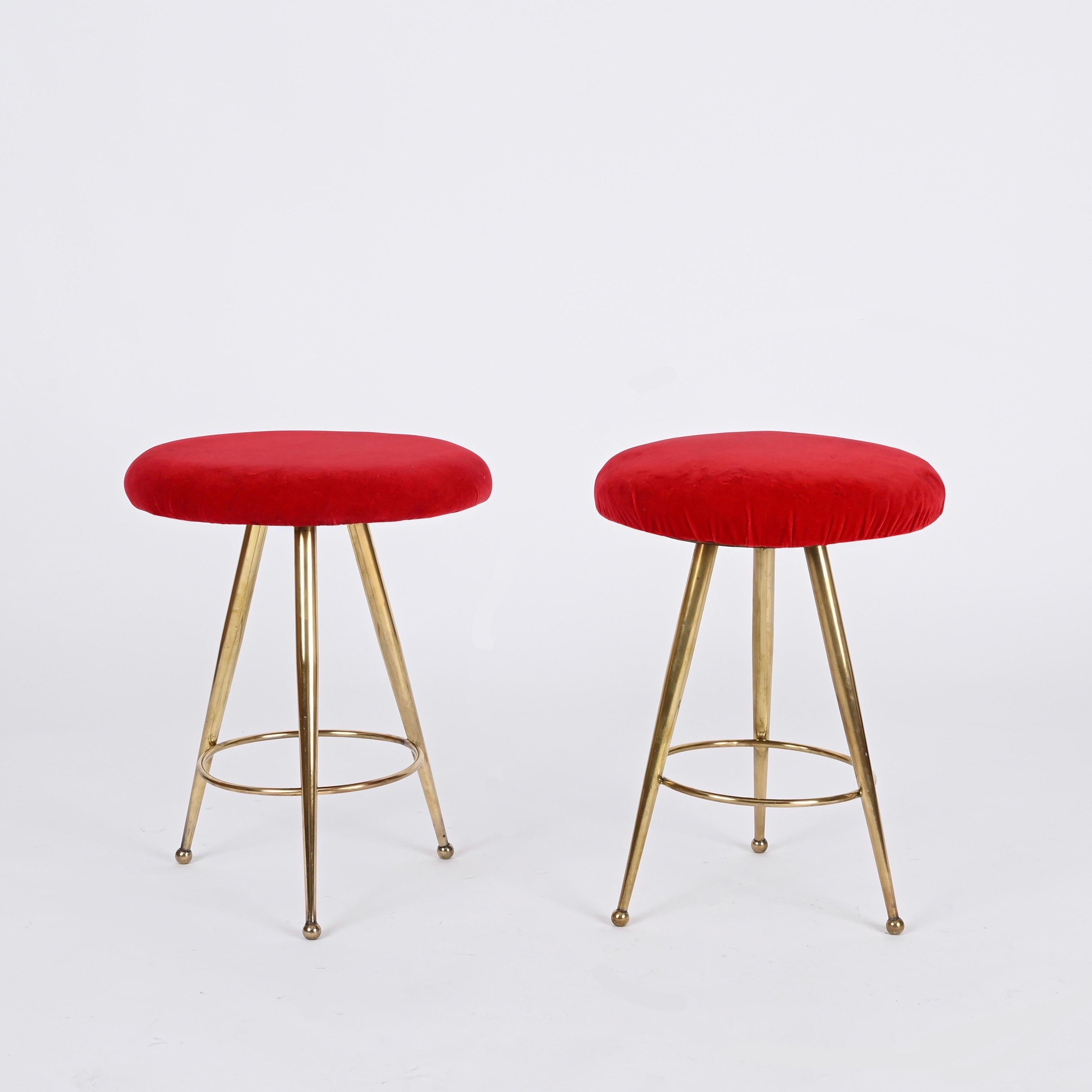 Gorgeous pair of Italian stools in golden brass and red velvet produced in Italy during the 1950s, clearly in the style of Gio Ponti.

In amazing condition, these stools are an elegant example of mid-century design, featuring a tapered three-legged
