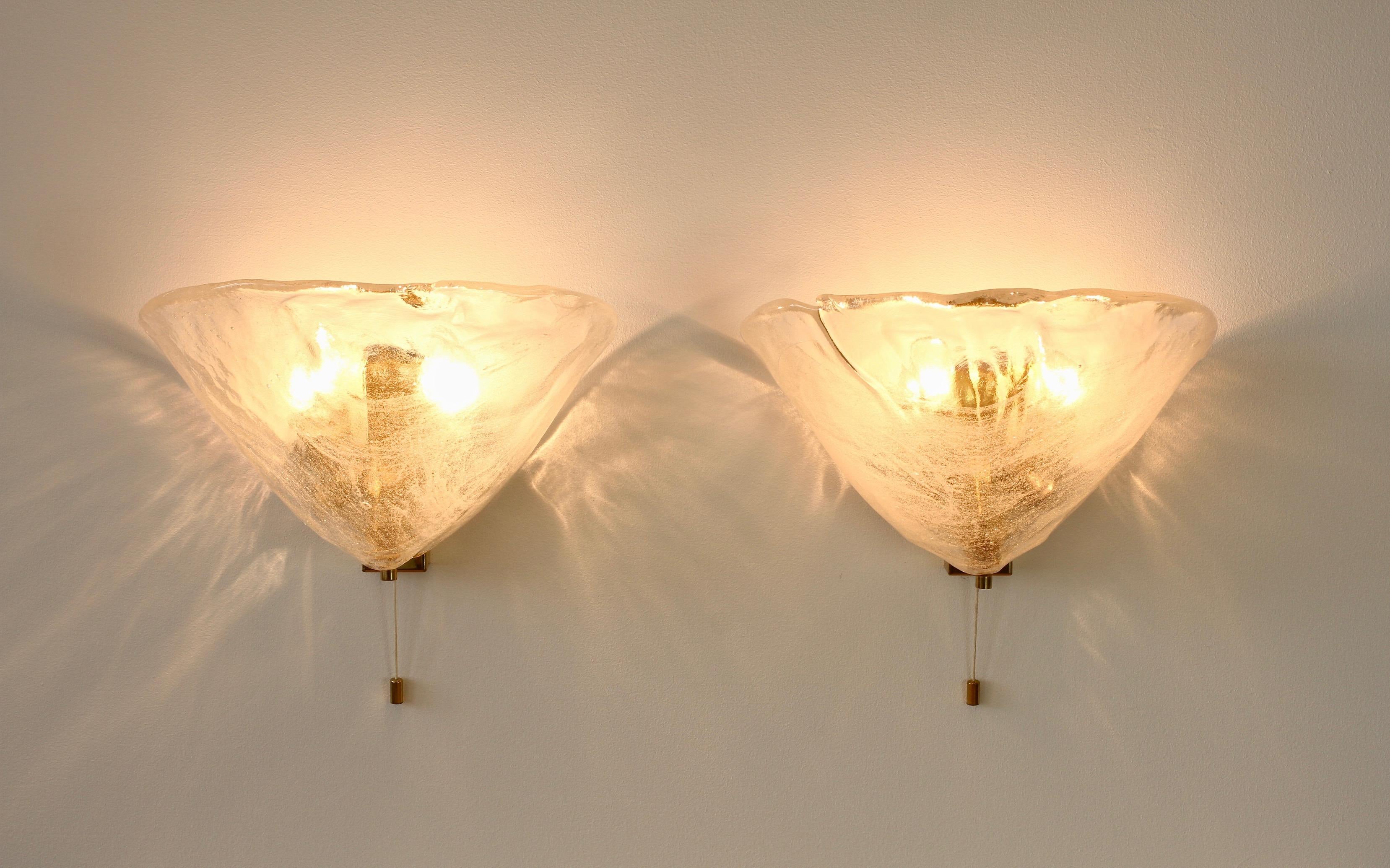 Large, elegant and rare pair of Austrian made melting ice glass wall sconces by Kalmar, circa 1960. Featuring two flower petal shaped glass elements, made by Italian Murano glass maker Mazzega, suspended on 24-karat gold-plated / gilt brass flush