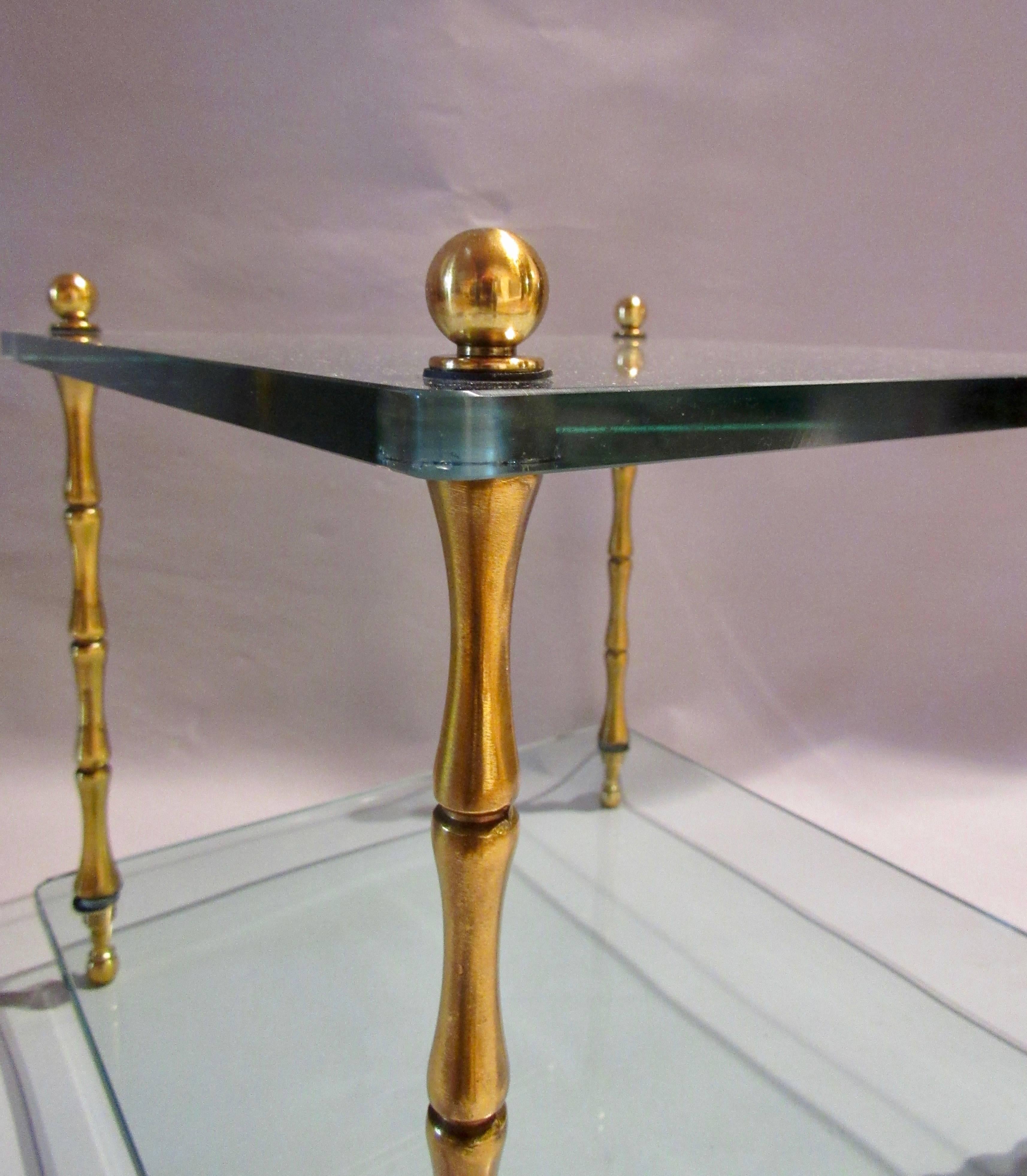 Baker Furniture Company pair of faux bamboo brass two-tiered glass top side tables in bronze lacquer. 
Modulating cast metal supports add a classical twist to these understated tables. 
The end tables have their original glass tops 5/8ths inch thick