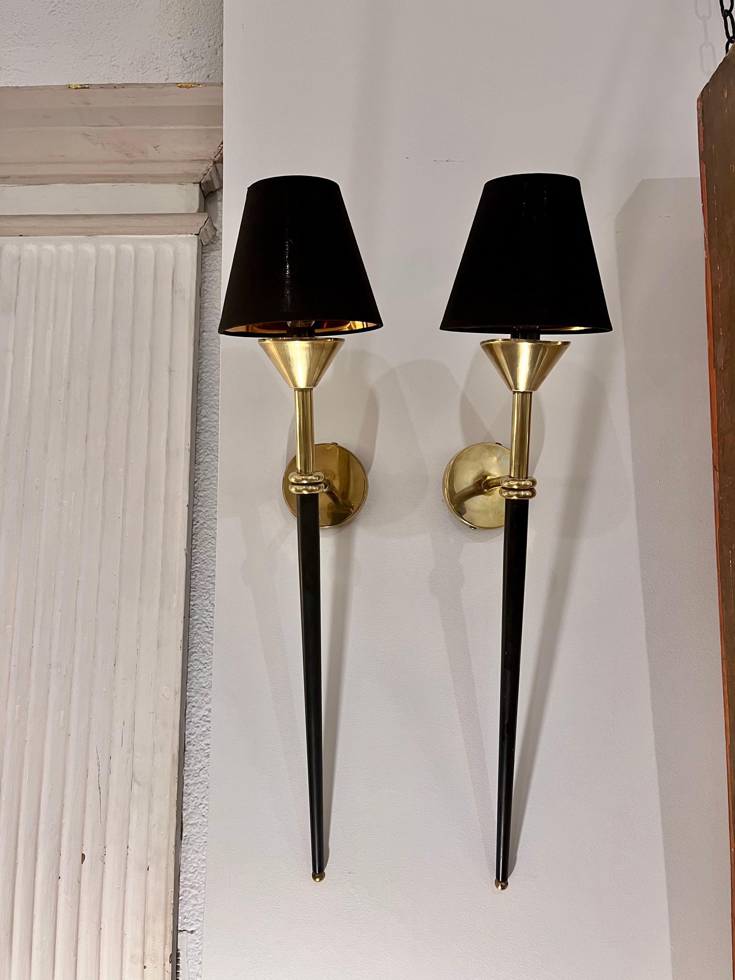 Coppia di grandi applique degli anni '50, attribuite alla Maison Lunel, in ottone dorato e metallo laccato, a forma di torcia, con paralumi in seta nera e interni dorati.