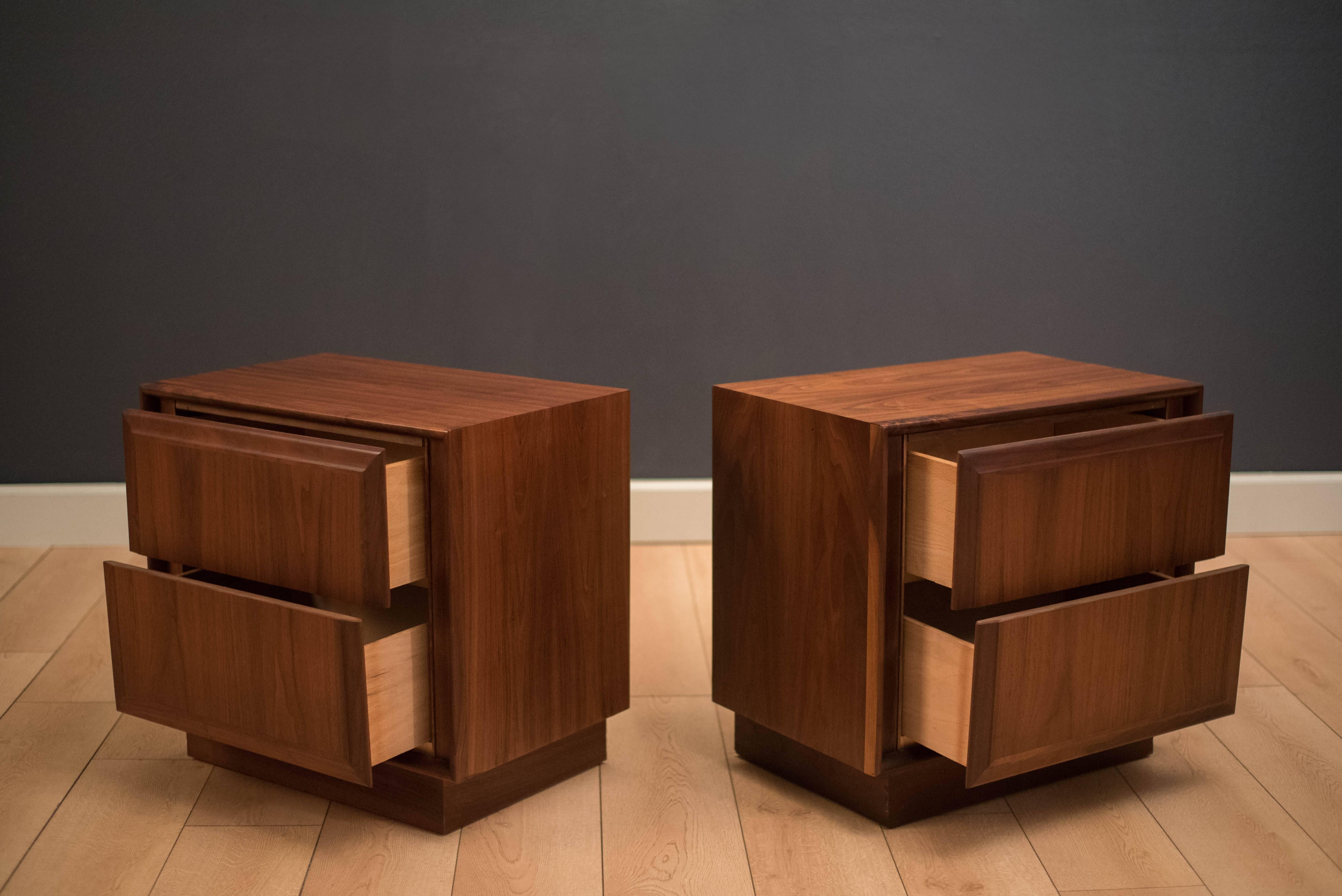 Mid-Century Modern pair of nightstands in walnut manufactured by Dillingham Furniture. This set includes plenty of storage with two dovetailed drawers each. Display a natural walnut finish and sits on an inset plinth base. Price is for the pair.